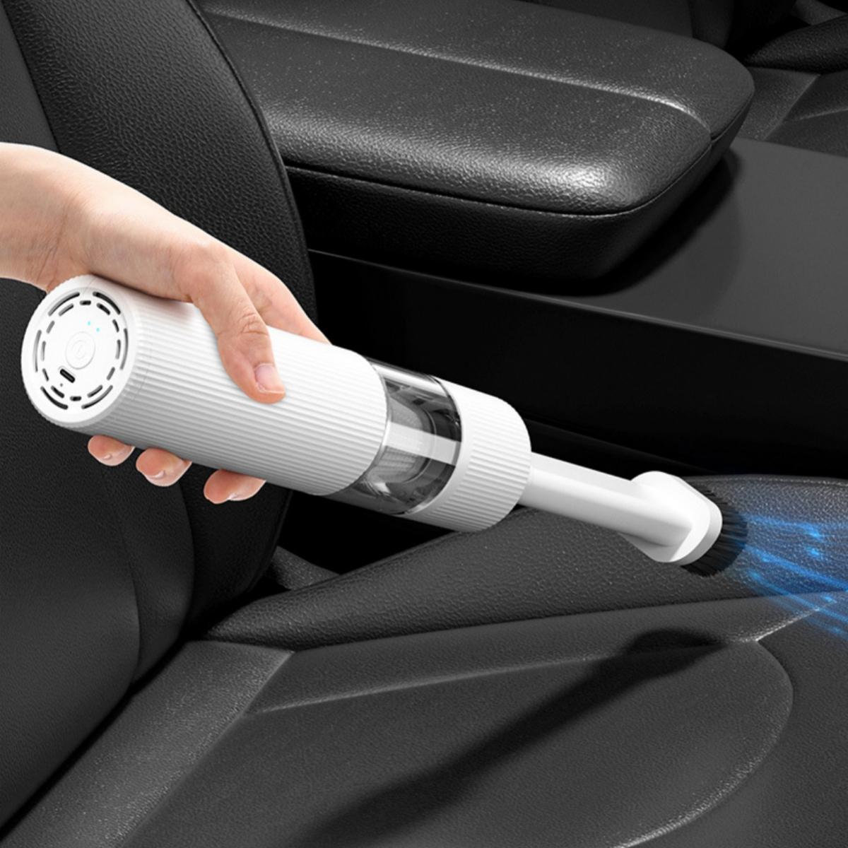 Eine Hand hält einen weißen Autostaubsauger mit Schlauch. Der Hintergrund ist ein Autositz.