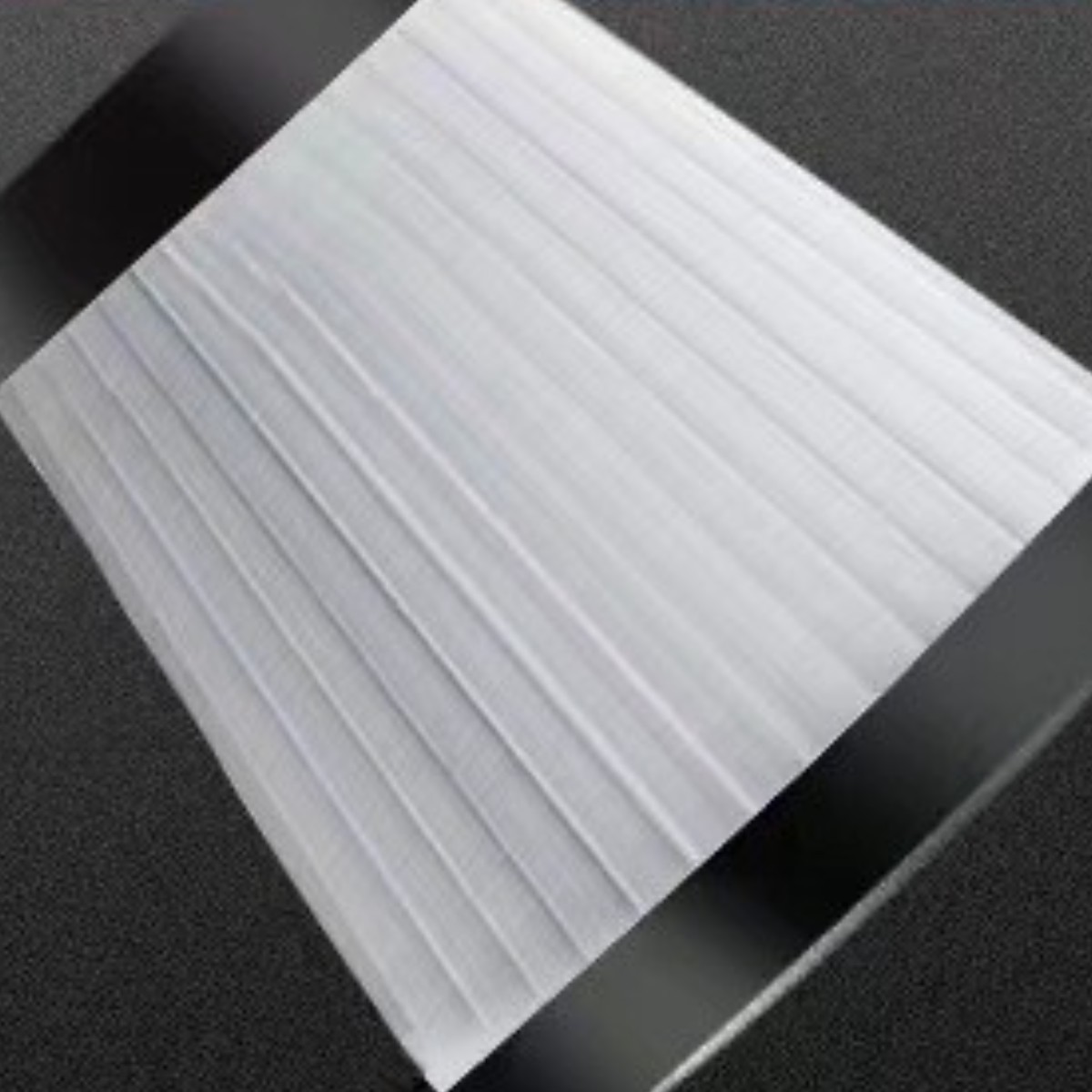 Weißes Material mit vertikalen Linien, leicht abgewinkelt, auf dunkler Oberfläche.