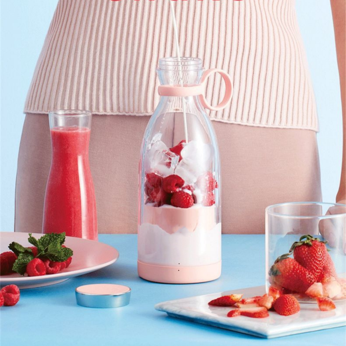 Mixer mit Zutaten: Himbeeren, Milch, Eis und eine Erdbeere.