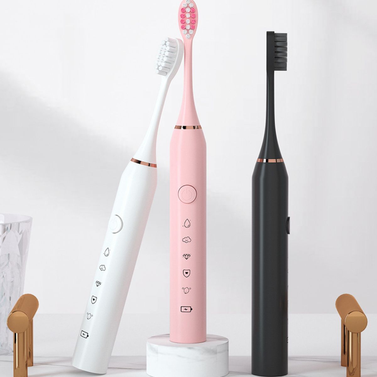 Drei elektrische Zahnbürsten: weiß, rosa und schwarz. Sie stehen auf einer Oberfläche.