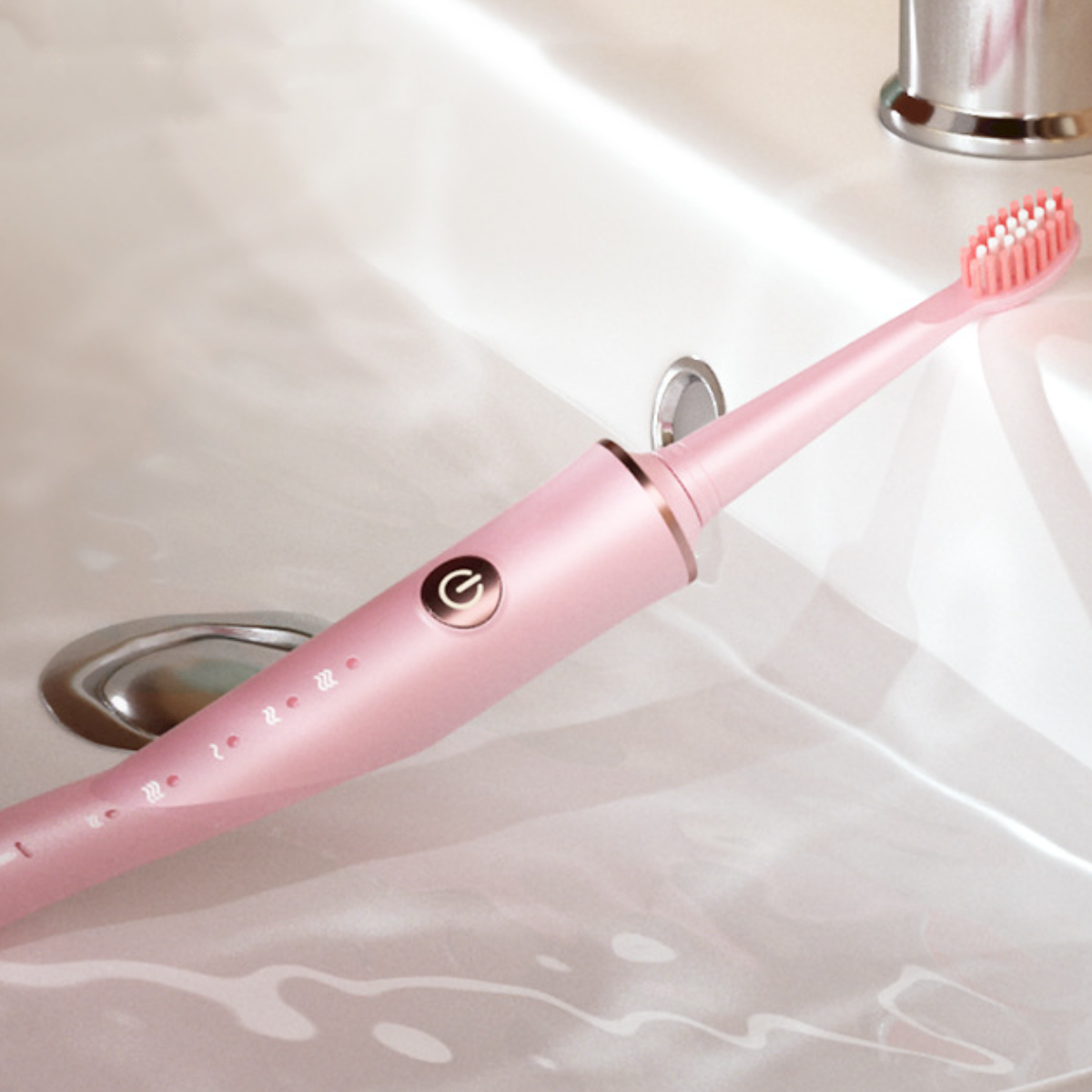 Eine rosa elektrische Zahnbürste liegt auf einem weißen Waschbecken, der Ein-Aus-Knopf leuchtet.