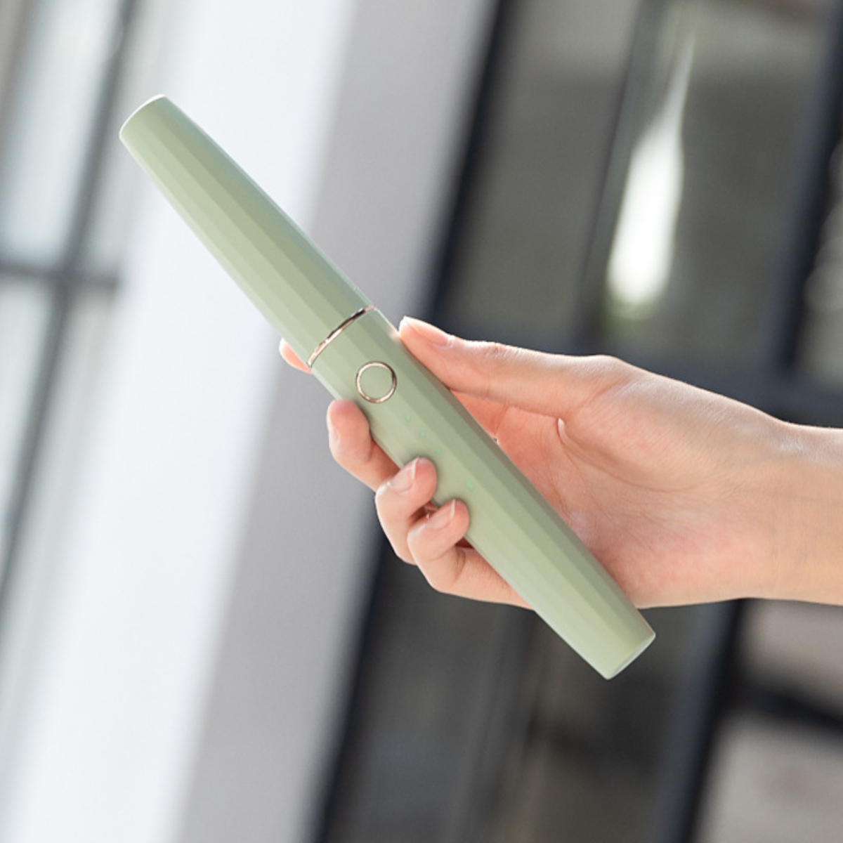 Eine Hand hält eine grüne elektrische Zahnbürste mit silbernem Knopf und hellgrünem Gehäuse.