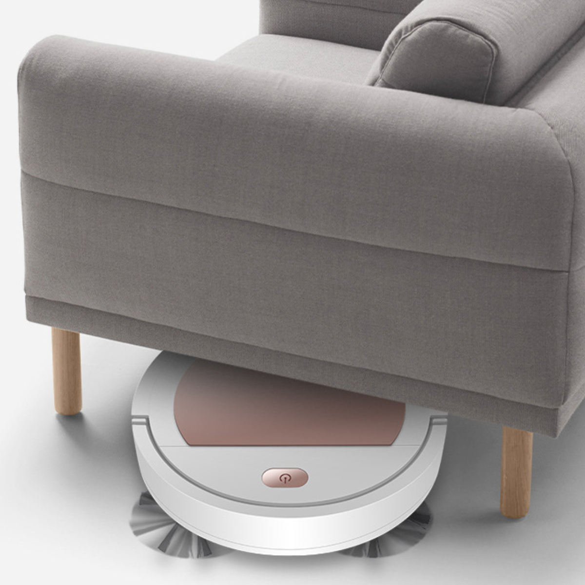 Roboter-Staubsauger unter einem grauen Sofa mit Holzbeinen. Er steht auf hellem Boden.