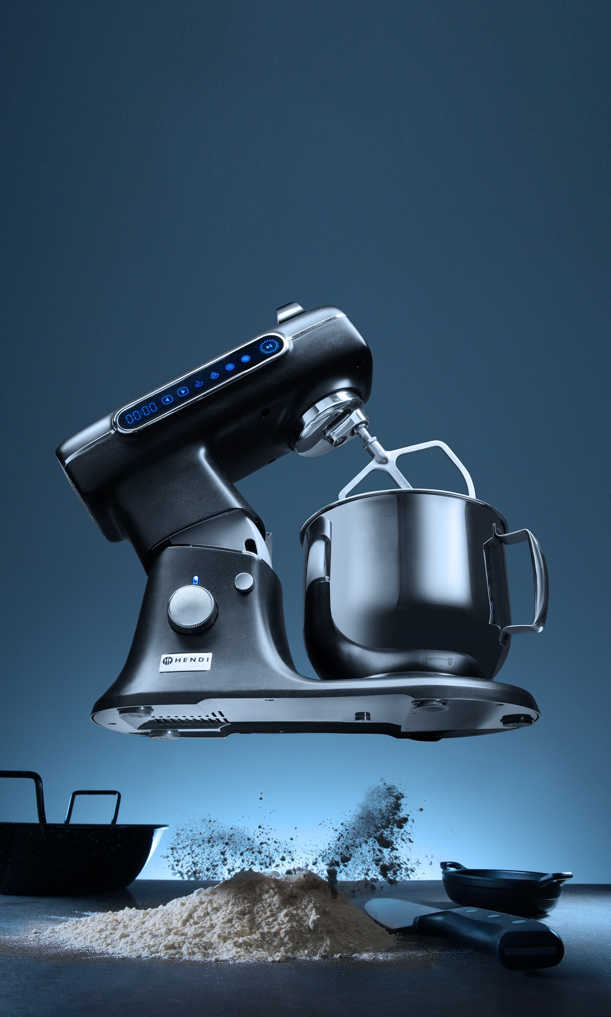 Schwarzer Küchenmixer mit Knethaken. Mehlhaufen und Schüssel vor blauem Hintergrund.