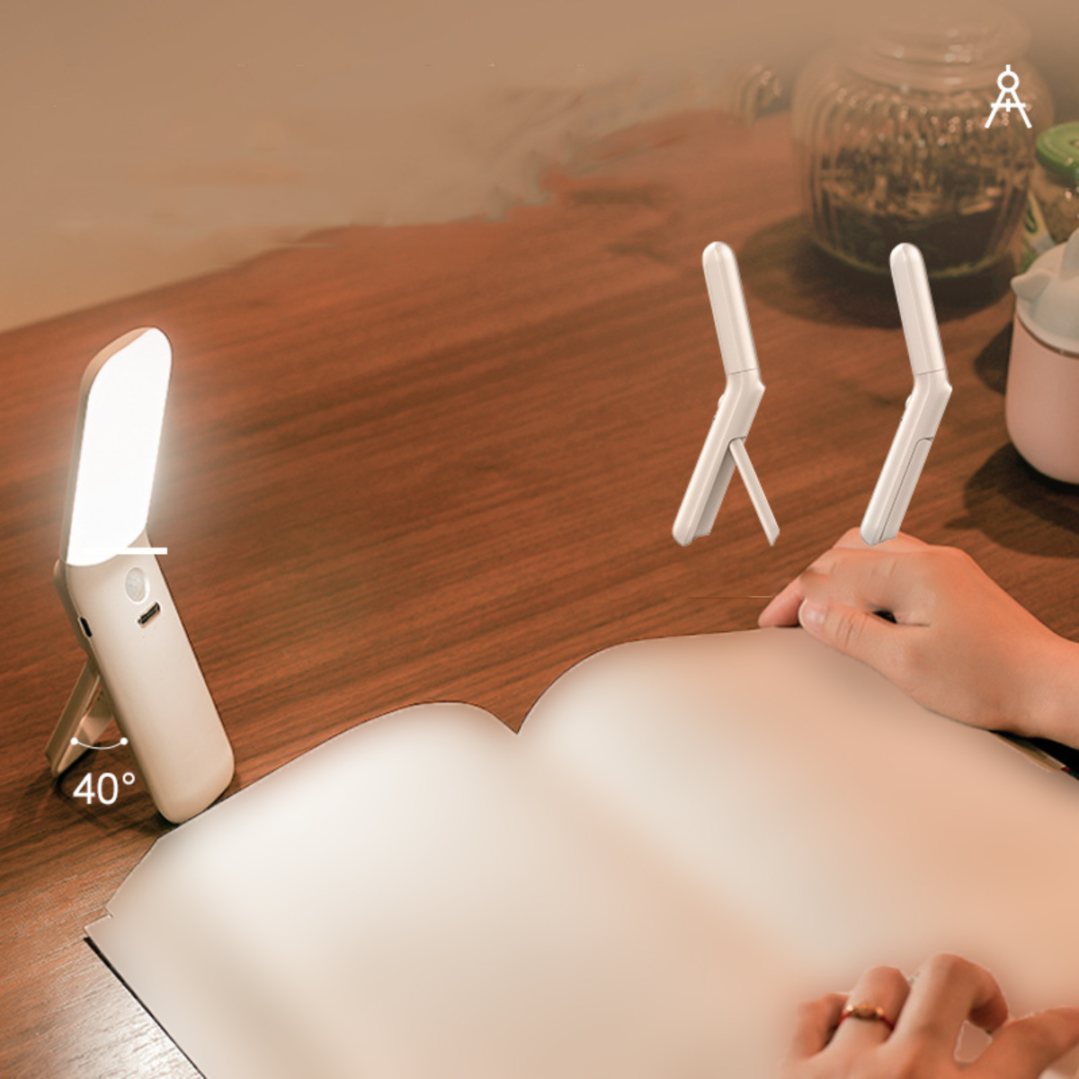 Weiße, faltbare LED-Lampe auf dem Schreibtisch, zwei weitere gefaltet. Hand, Buch, Objekte.