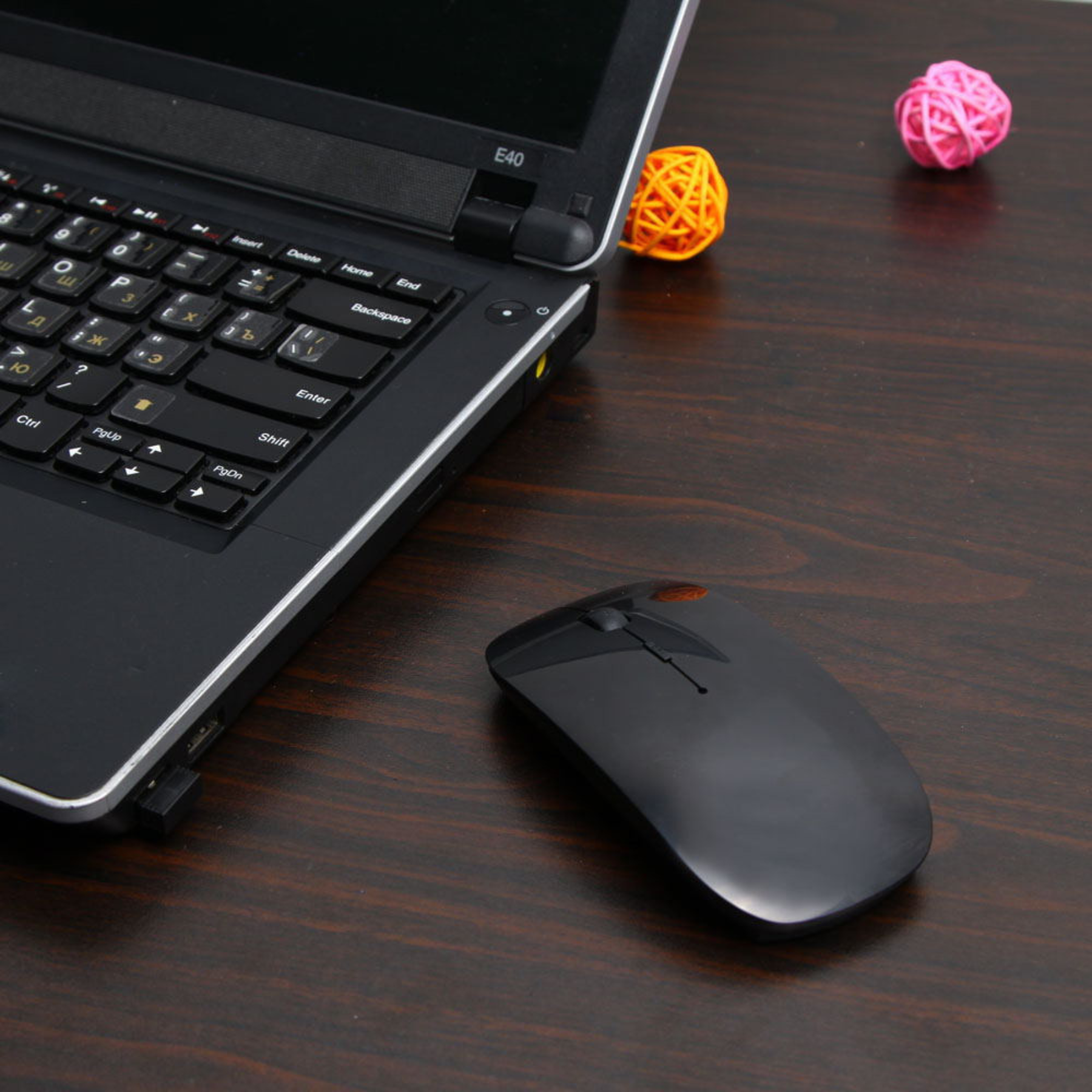 Ein schwarzer Laptop und eine Maus auf einem dunklen Holzschreibtisch. Zwei dekorative Kugeln sind ebenfalls sichtbar.