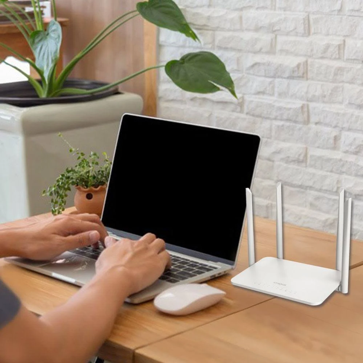 Una persona usa un laptop con un router bianco accanto, su un tavolo di legno.