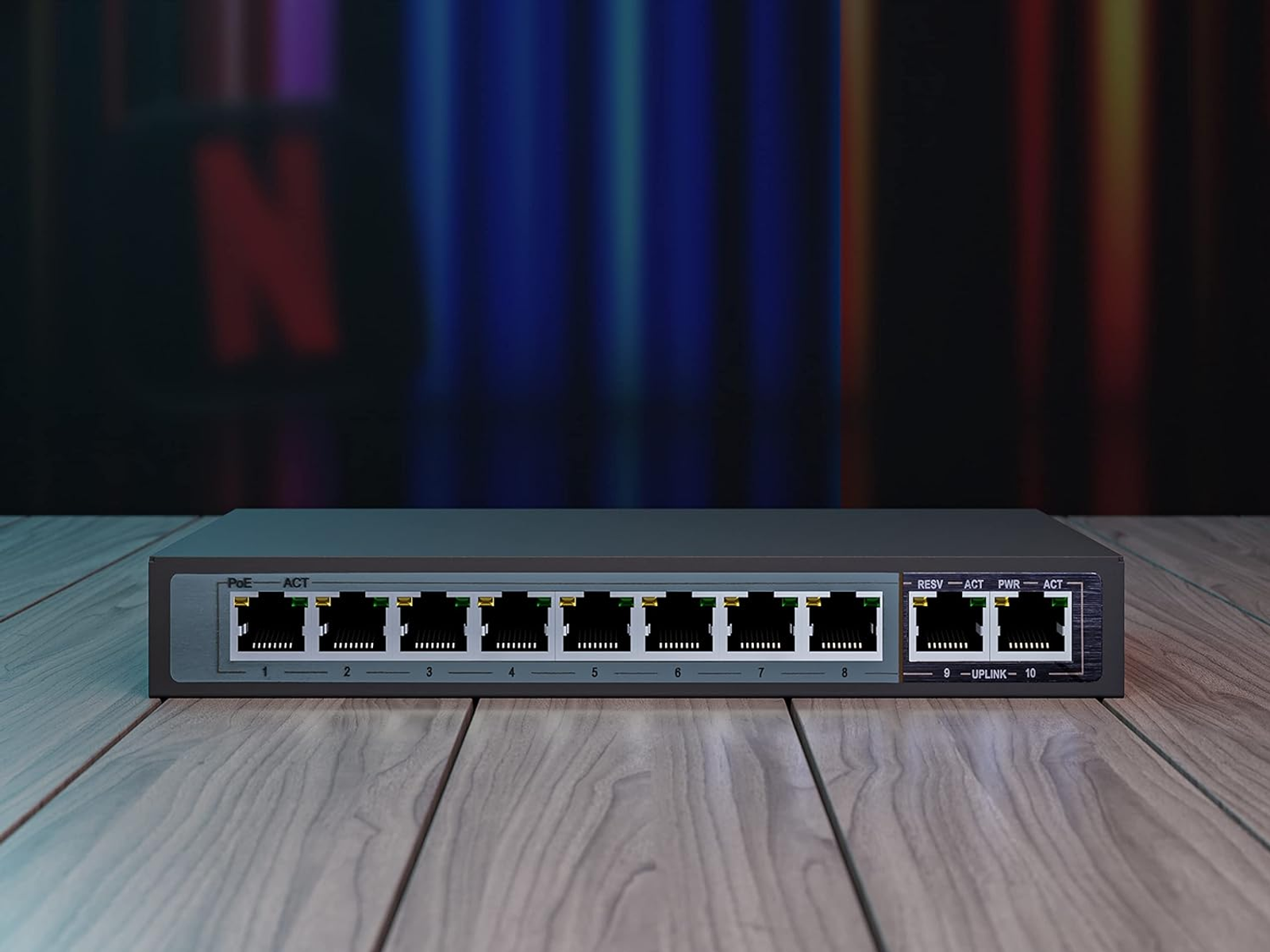 Switch di rete nero con 10 porte, su un tavolo di legno, con uno sfondo sfocato di schermo.