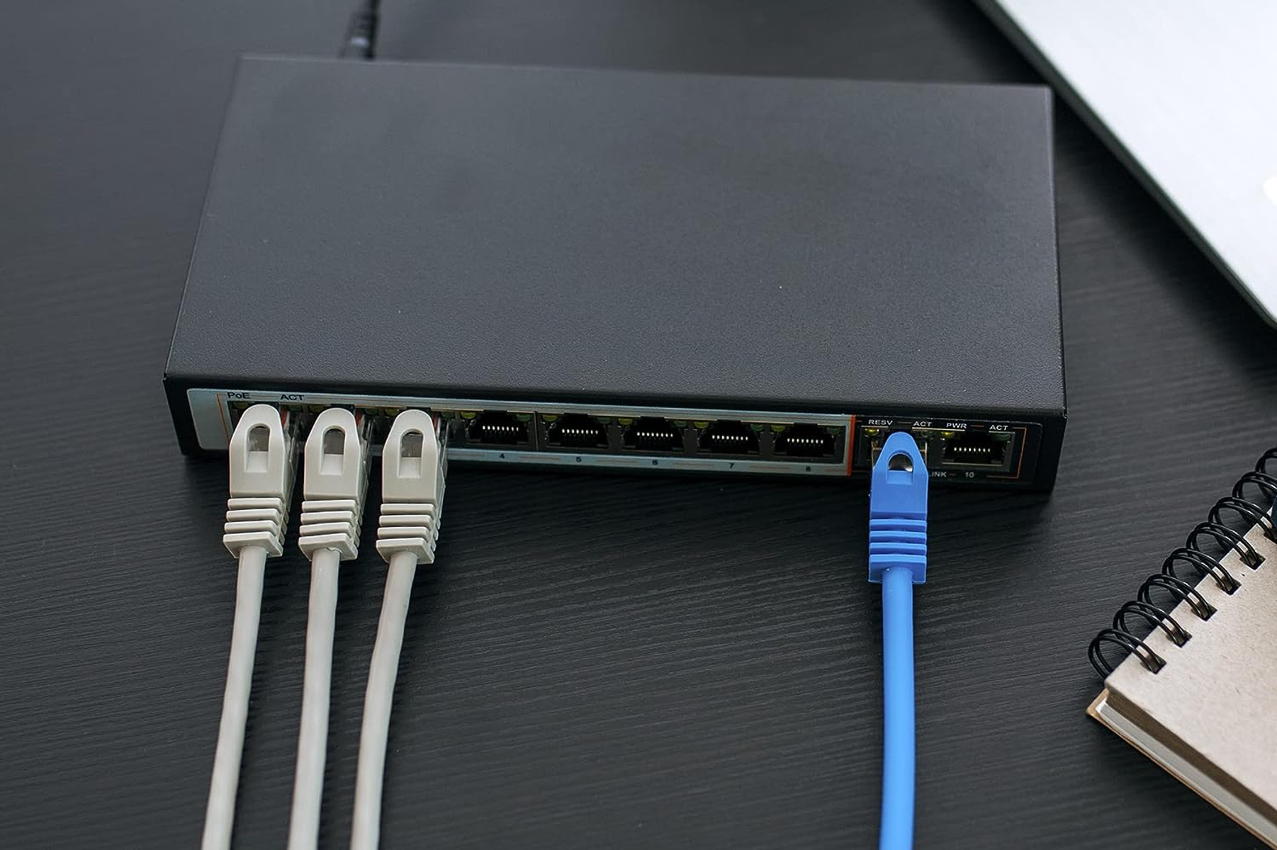 Switch di rete nero con cavi Ethernet collegati e un taccuino.