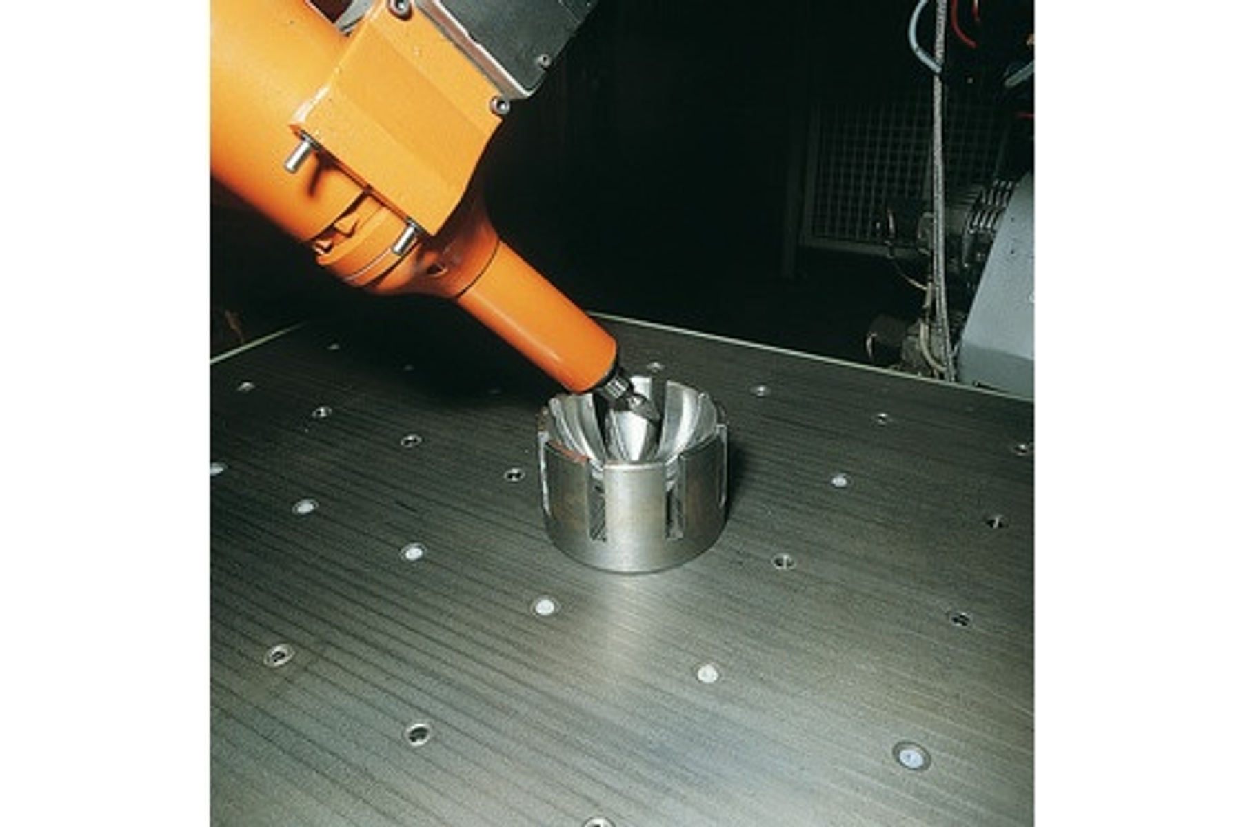 Industrieroboterarm bearbeitet ein Metallteil. Oranger Arm auf einem metallischen Tisch.