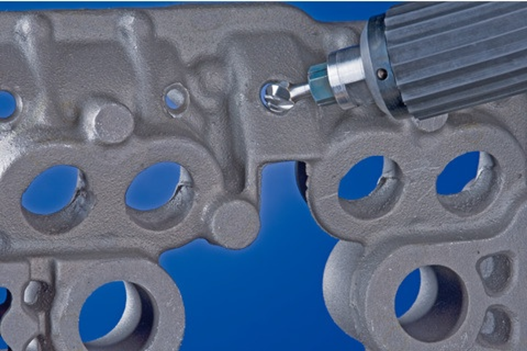 Ein Fräser schleift das Innere eines Metallteils mit Löchern. Blauer Hintergrund.