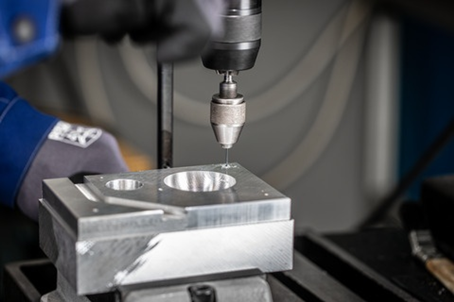 Nahaufnahme eines Bohrers, der in einen Metallblock bohrt, mit einer Bohrmaschine und Hand.