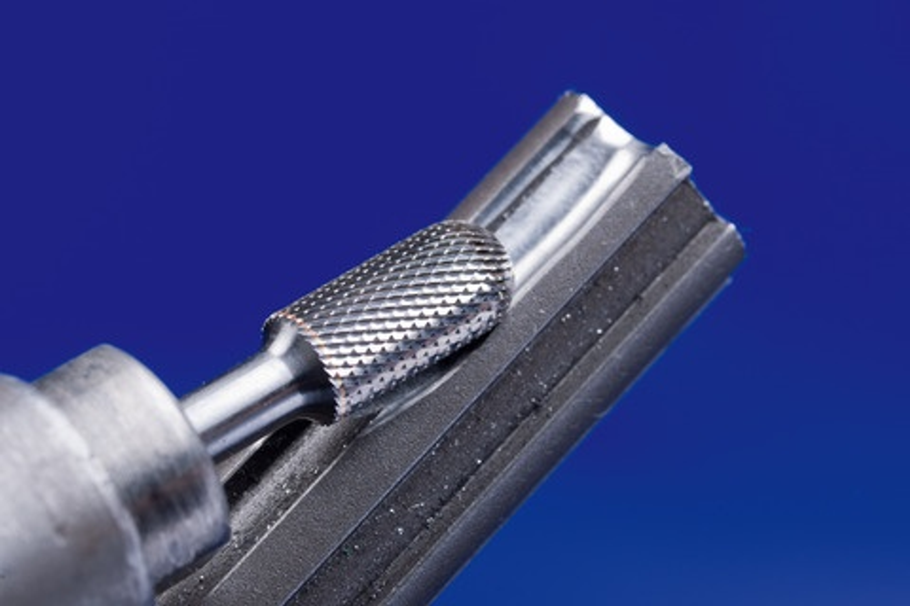 Ein Rotationsfräser in Aktion, der eine Nut in einem Metallstück bearbeitet. Hintergrund ist eine blaue Wand.