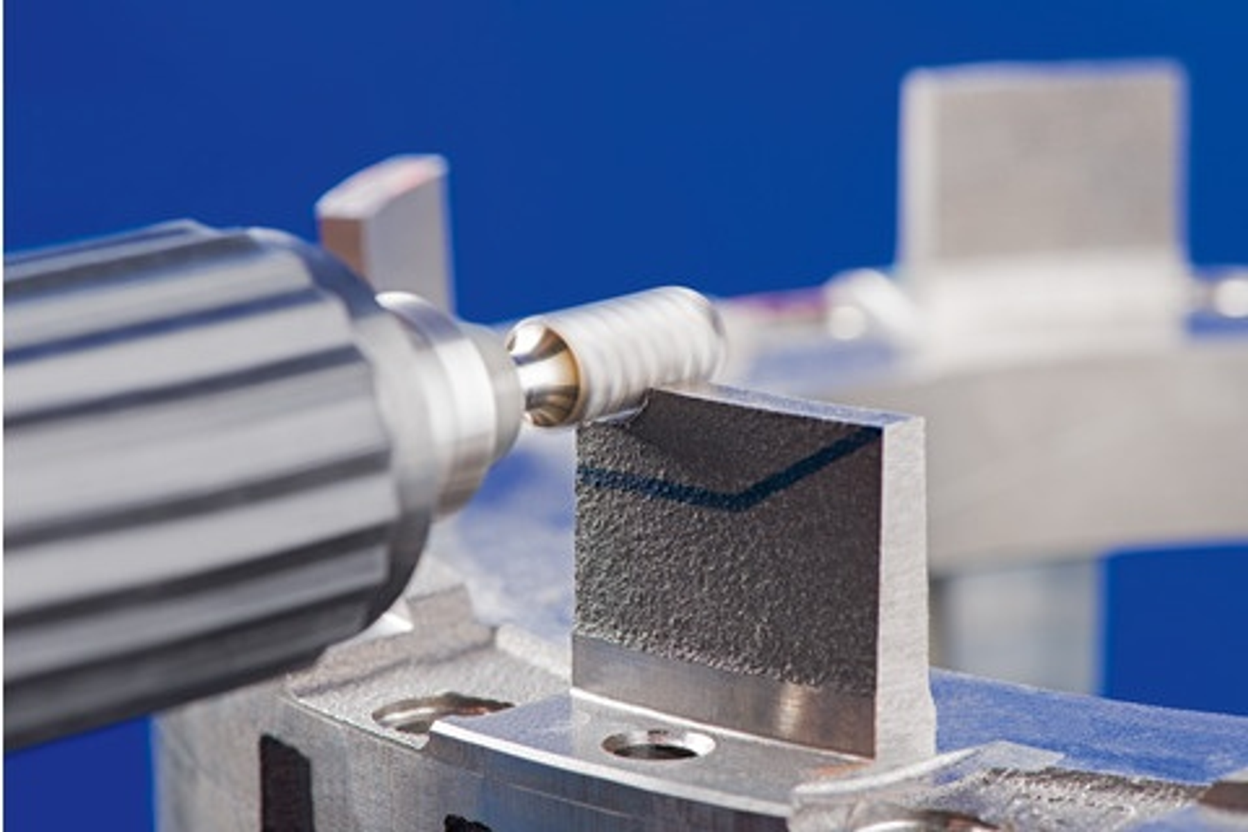 Ein Rotationsfräswerkzeug bearbeitet ein Metallteil. Das Werkzeug wird von einer Maschine gehalten. Der Hintergrund ist blau.