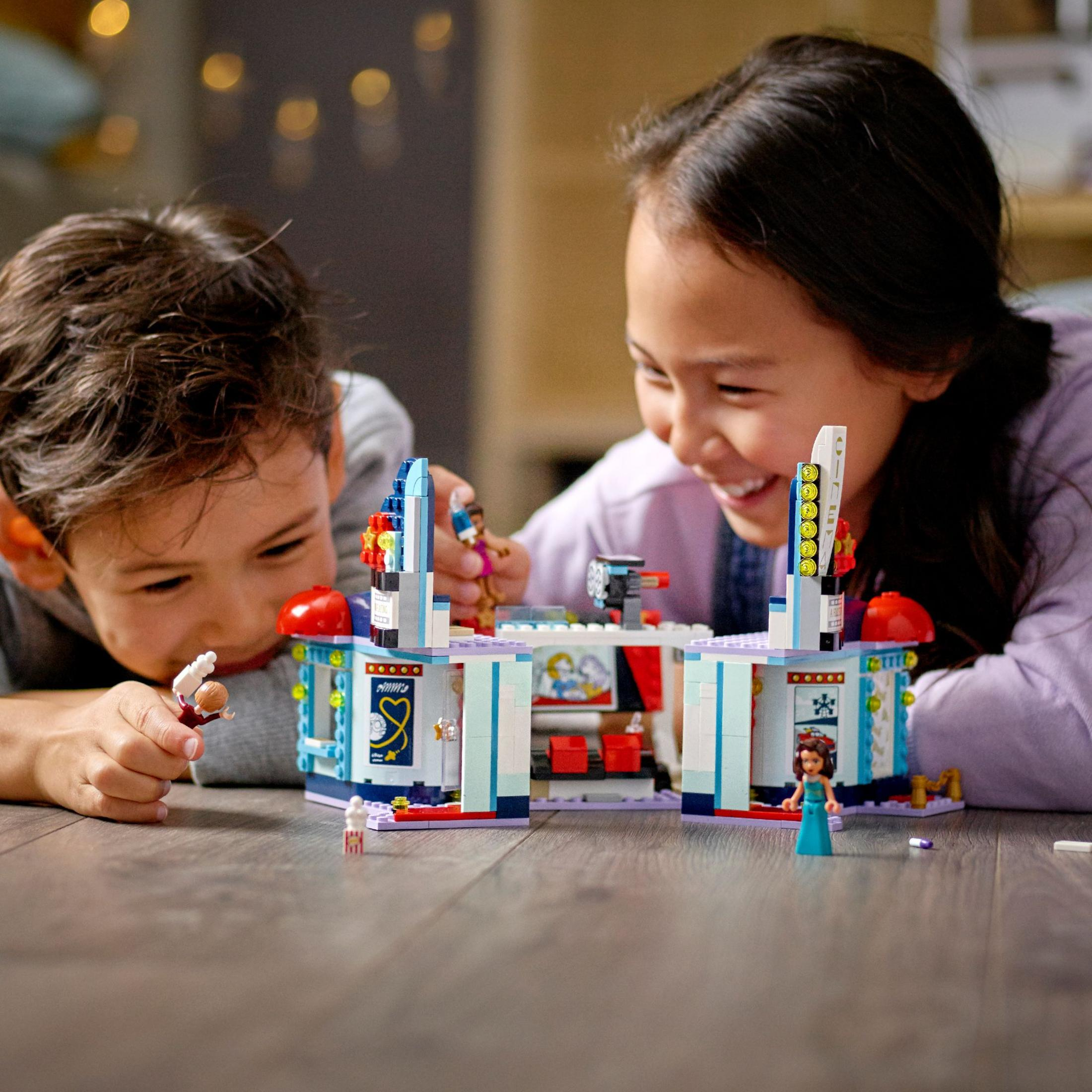 Dos niños jugando con un set de Lego en el suelo, construyendo un escenario colorido con figuras.