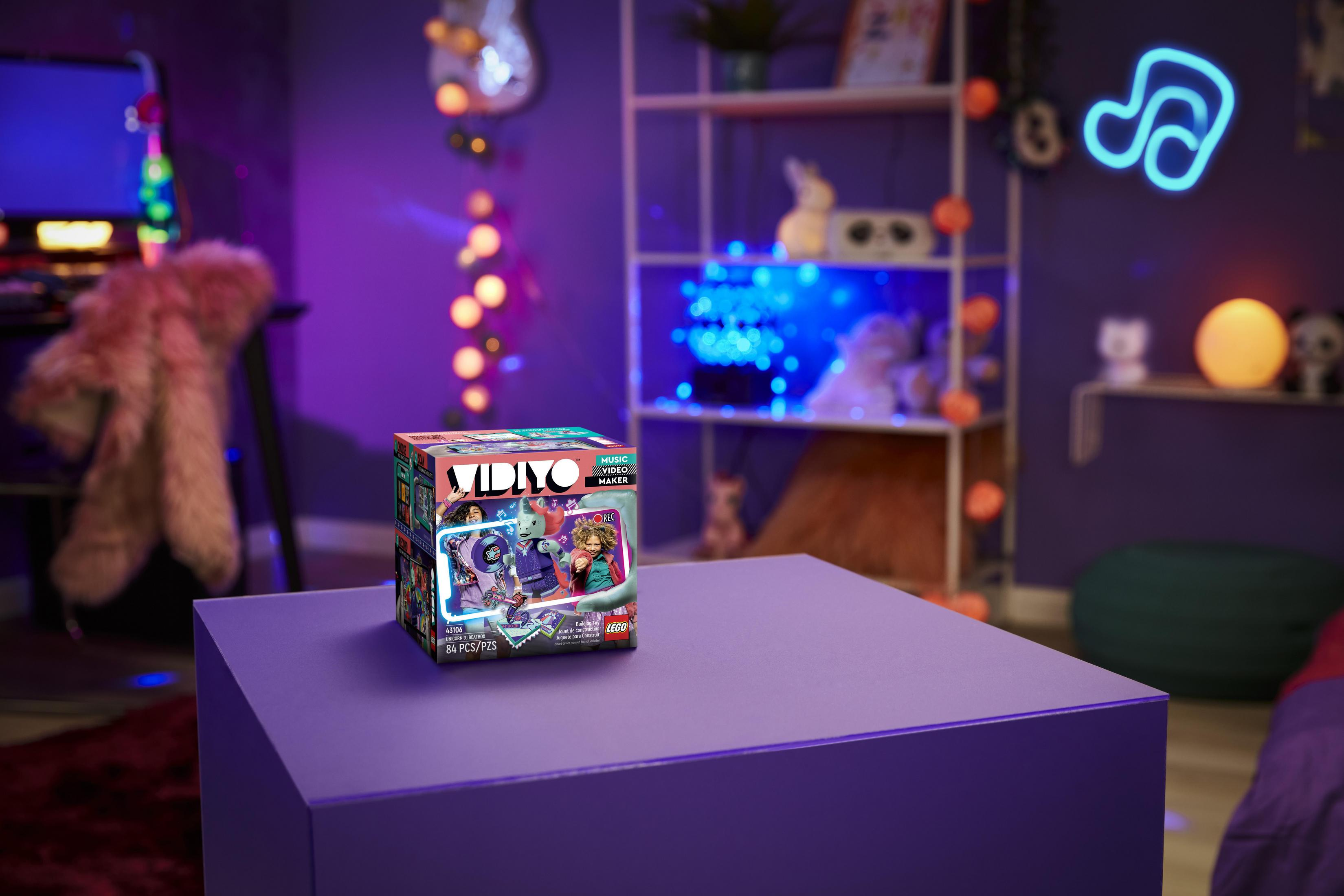 Pudełko LEGO na fioletowym stole w pokoju z dekoracjami. Neonowy znak w tle.