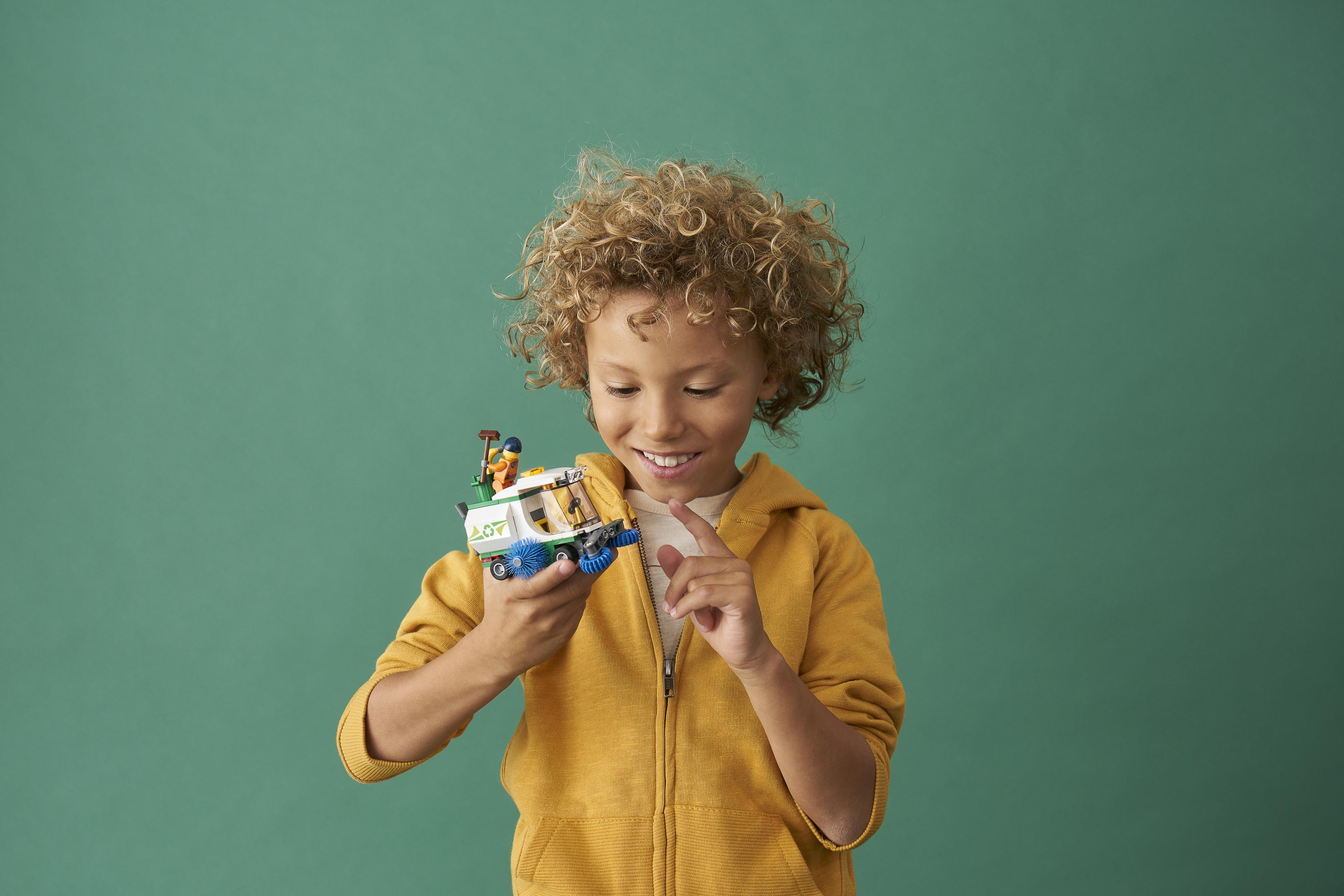 Ein kleiner Junge hält einen Spielzeug-LKW mit einer Lego-Figur oben drauf, auf grünem Hintergrund.