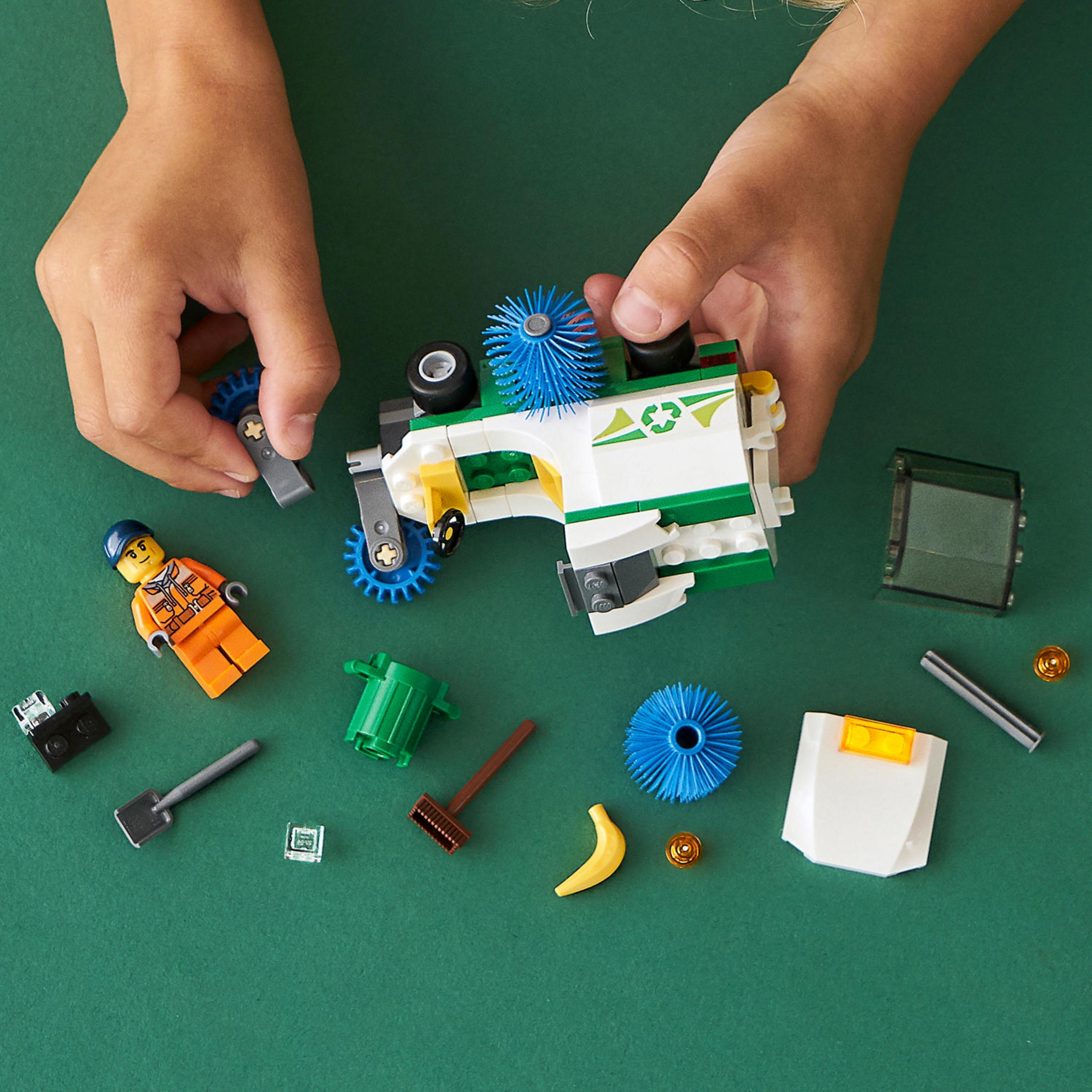 Hände spielen mit Lego-Spielzeug, darunter ein Müllwagen, eine Minifigur, eine Banane und andere Lego-Elemente.