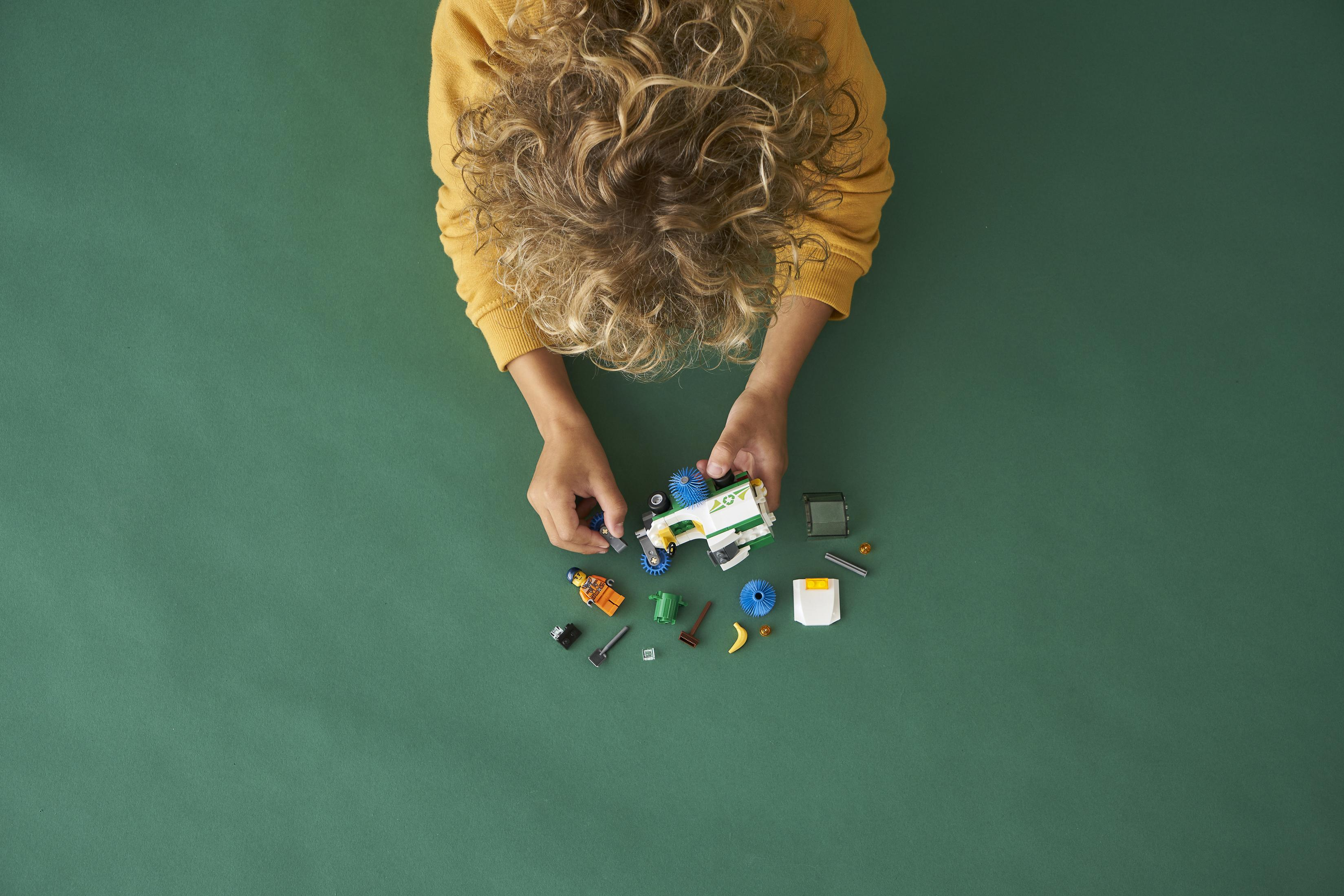 Kinderhände bauen ein Lego-Spielzeug auf grüner Oberfläche, Draufsicht.