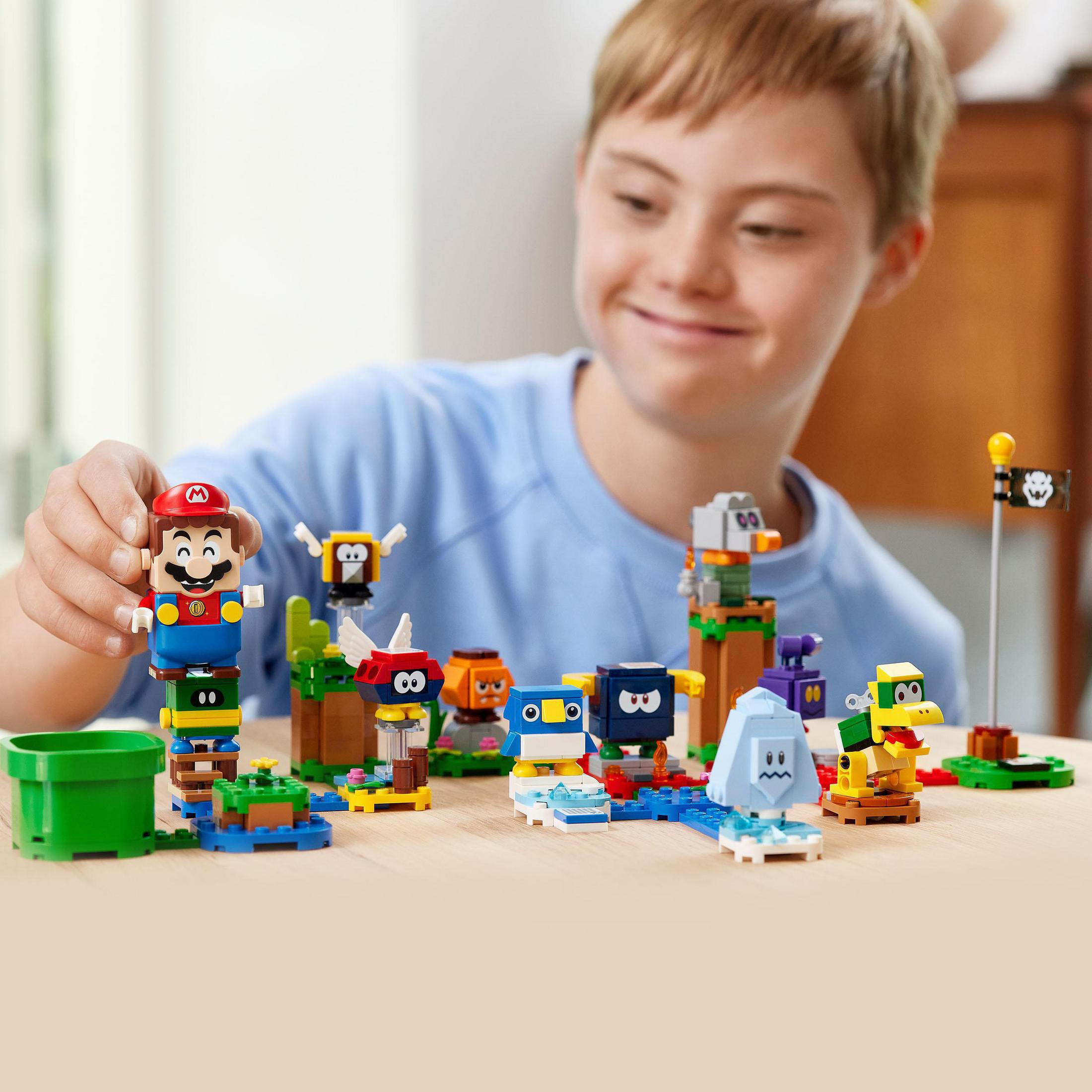 Down sendromlu genç bir çocuk, LEGO Mario setiyle oynuyor. Çeşitli figürler ve aksesuarlar.
