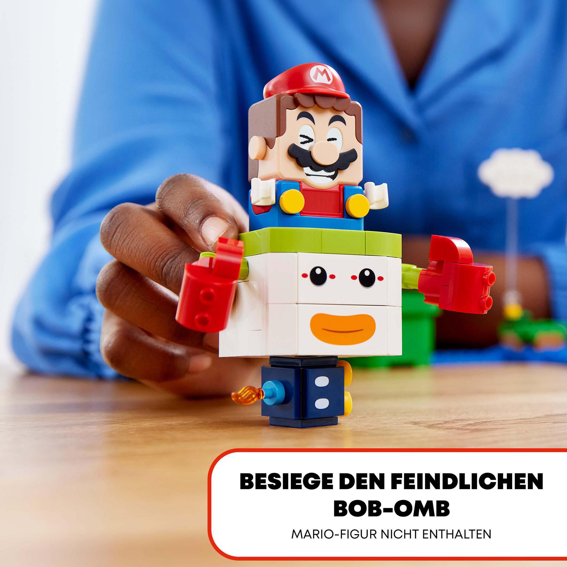 Lego Mario und ein Bob-omb-Spielzeug auf einem Holztisch. Der Text lautet 'Besiege den feindlichen Bob-omb'.