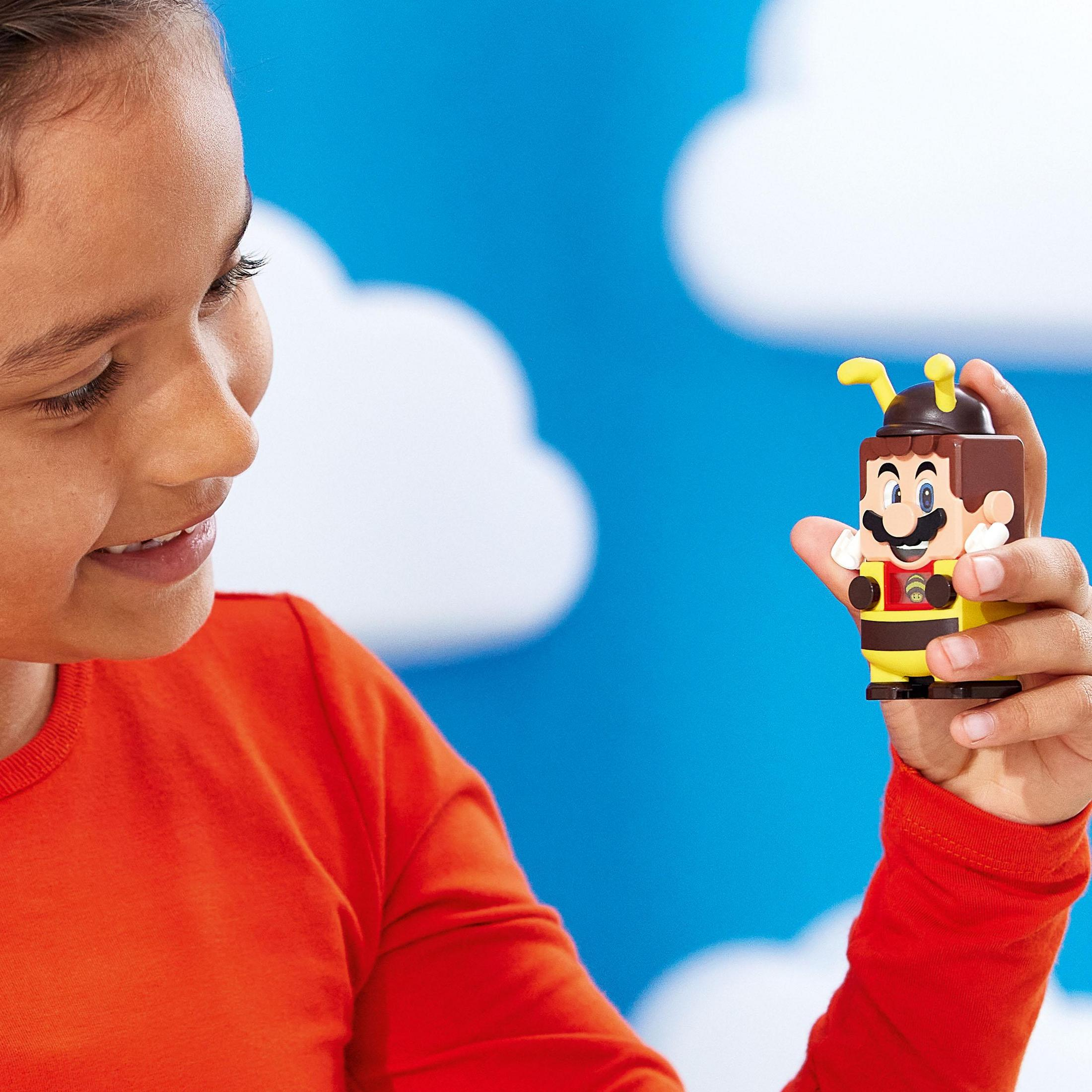 Un bambino che tiene in mano una figura LEGO di Mario con un costume da ape sorridente.