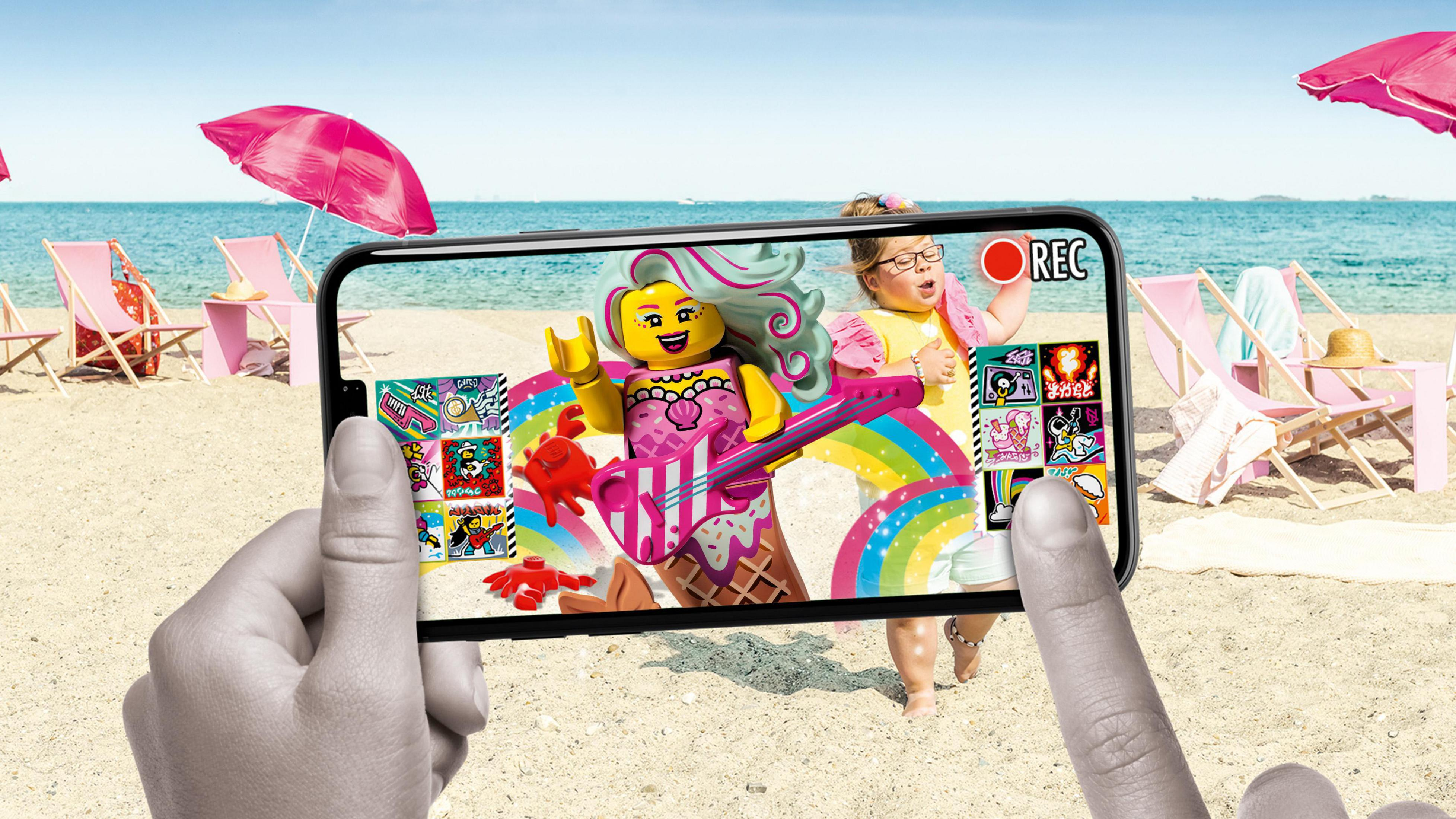 Osoba trzyma telefon z sceną LEGO z dziewczyną na plaży.