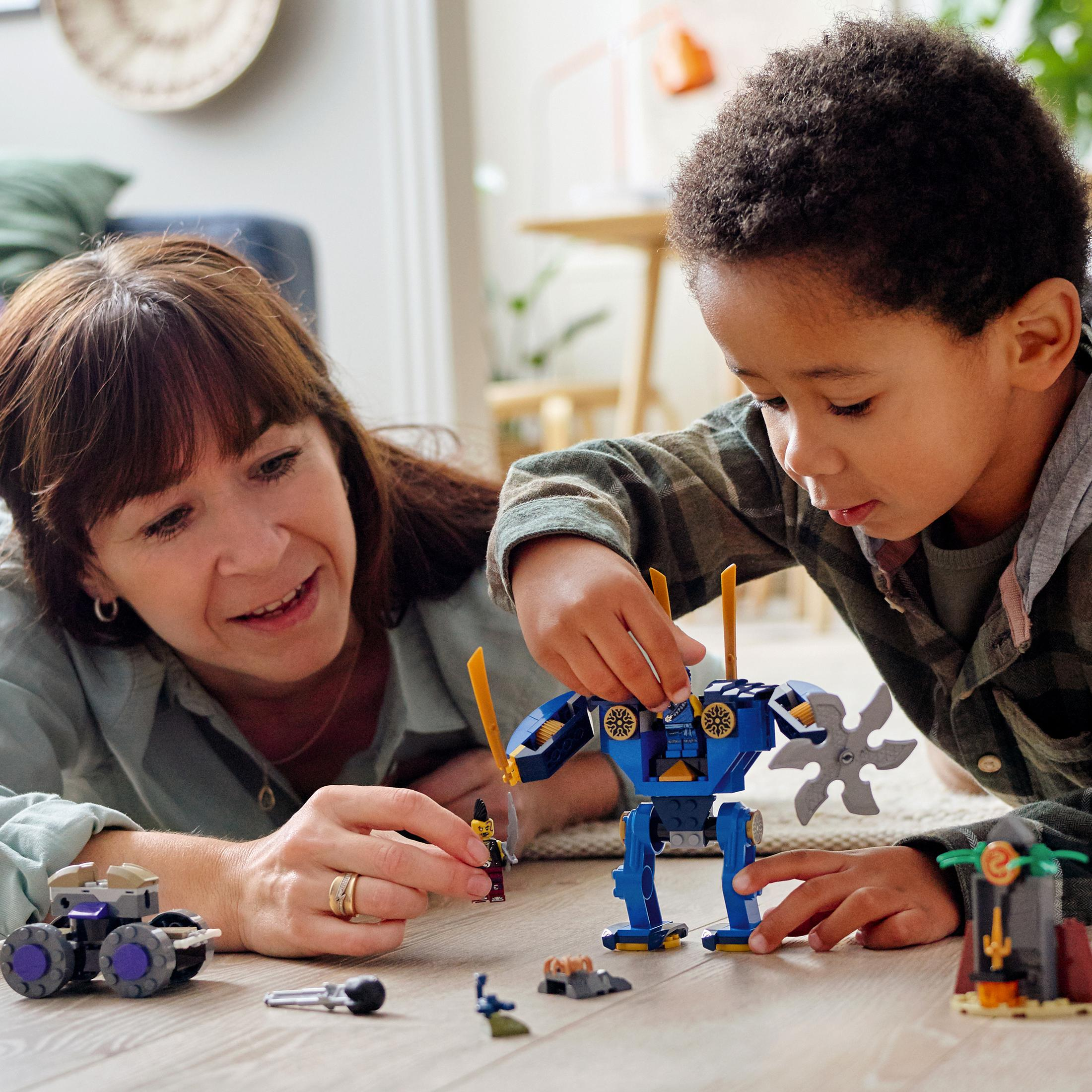 Kind und Frau spielen mit Lego. Lego Ninjago Set mit Roboter. Hellblauer Hintergrund.