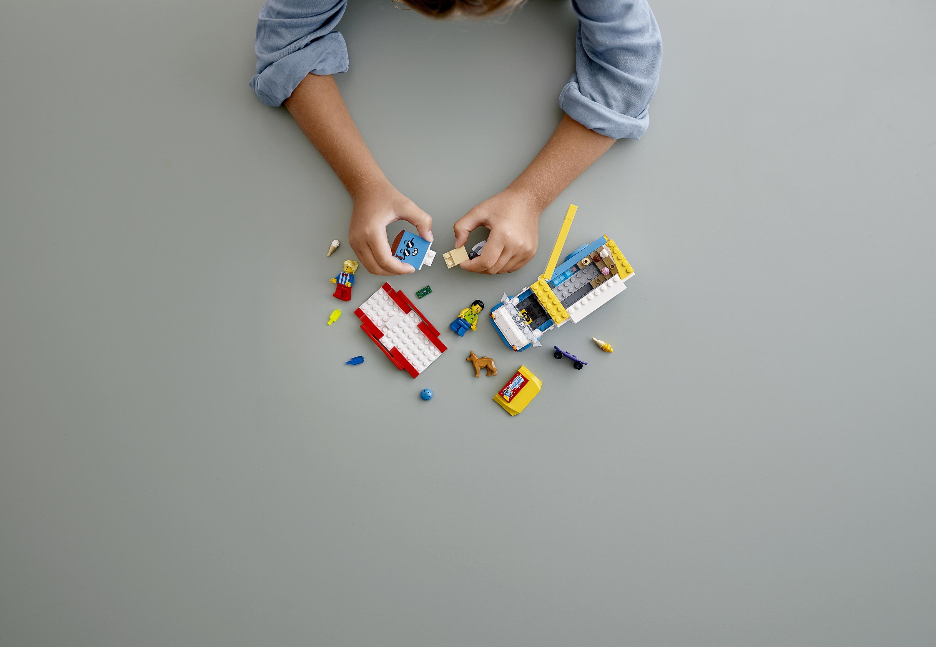 Kinderhände bauen einen Lego-Eiswagen auf grauer Oberfläche zusammen.