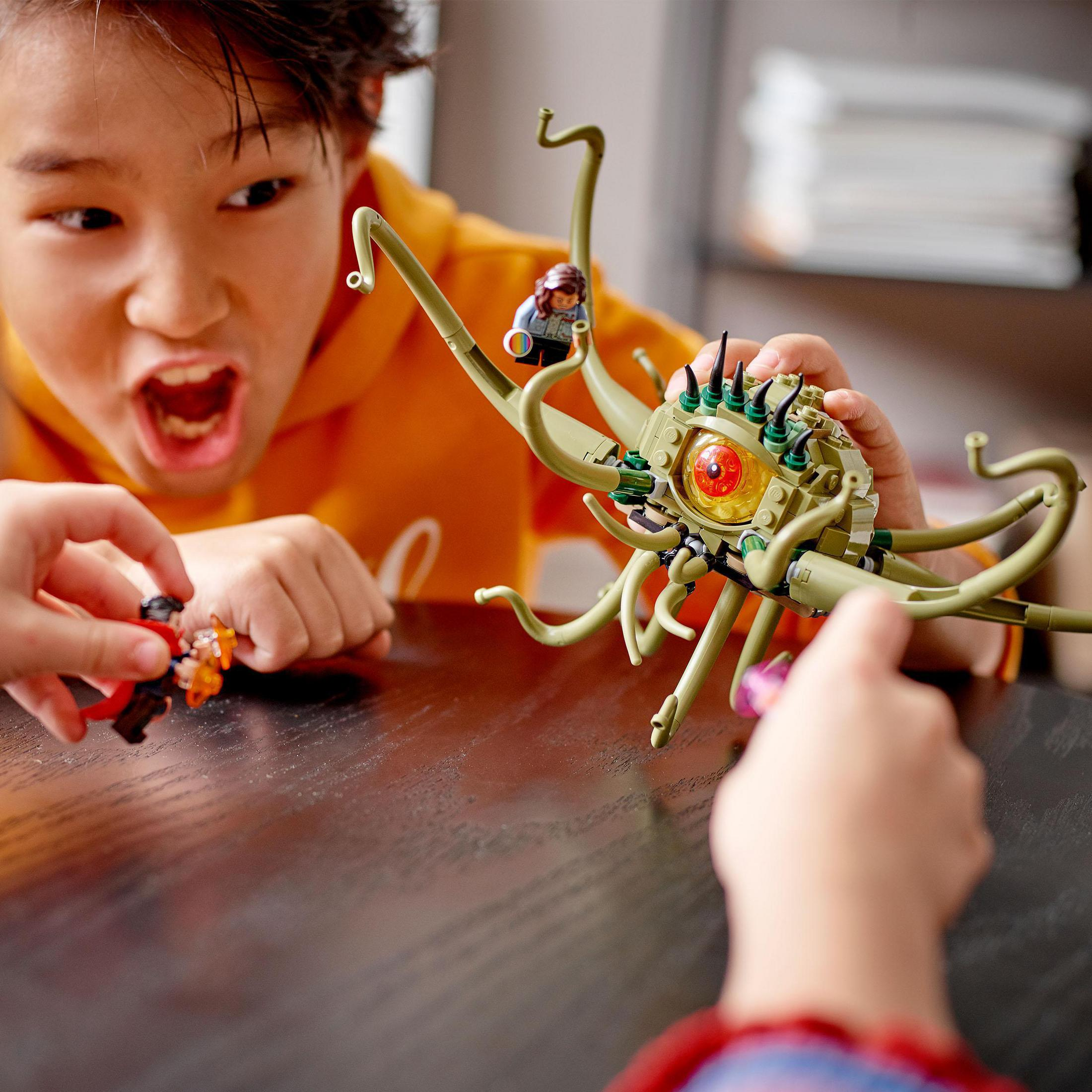 Junge und eine Person spielen mit Lego-Monster. Junge ist aufgeregt. Dunkler Holztisch.