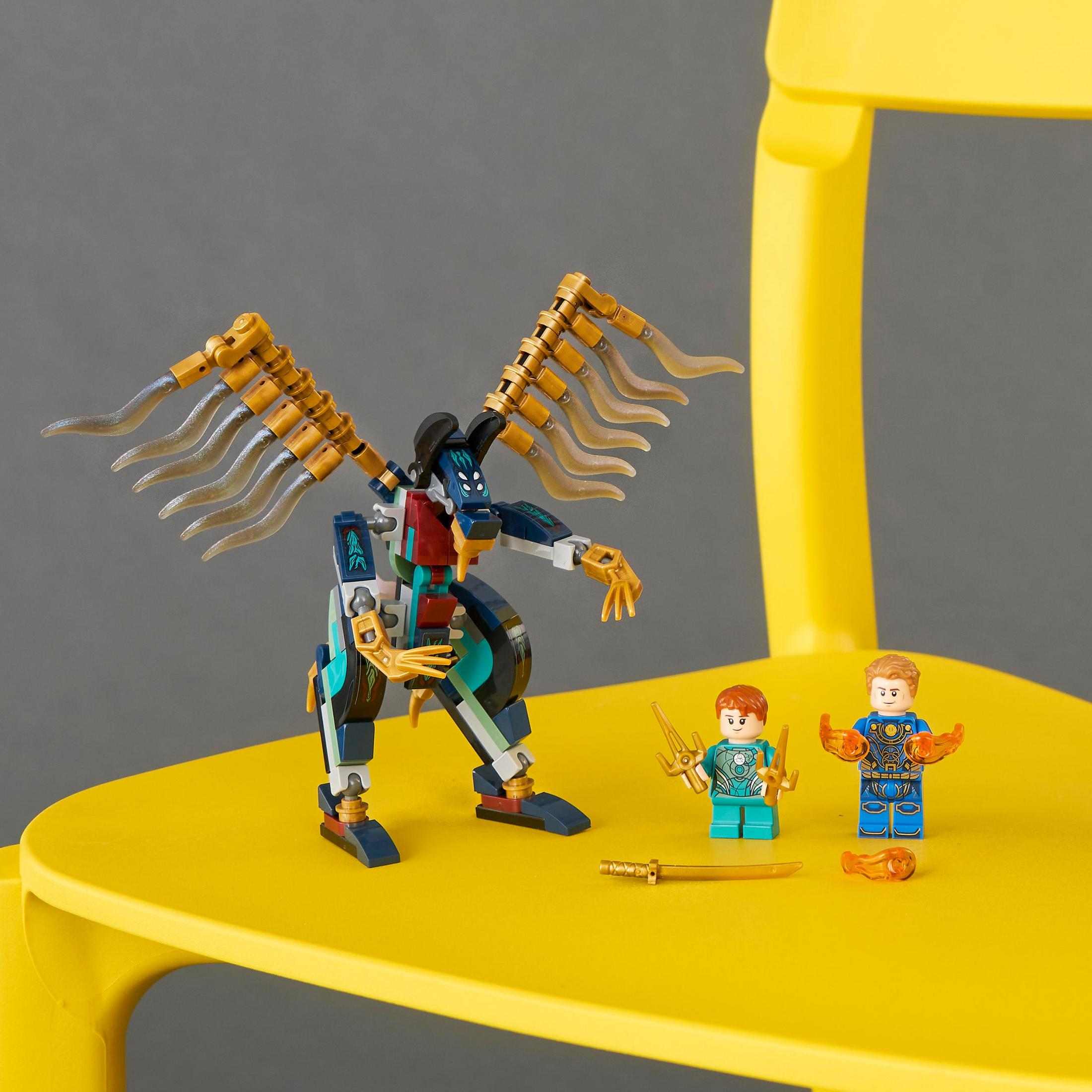 Lego-Set mit einer Roboterfigur und zwei kleineren Figuren auf einem gelben Stuhl. Es gibt auch Waffen.