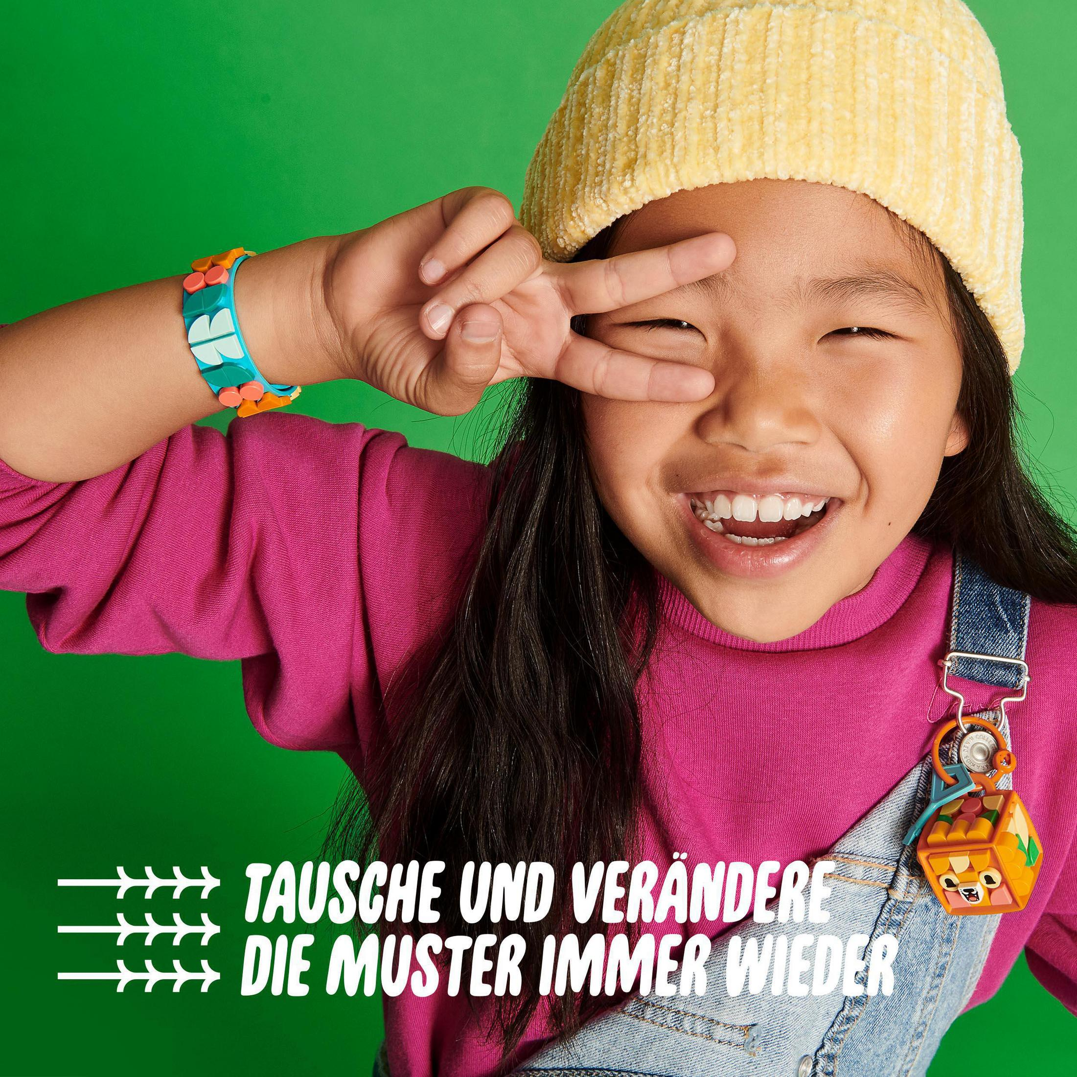 Une jeune fille souriante faisant le signe de paix. Elle porte une chemise rose et une salopette en jean. Fond vert.