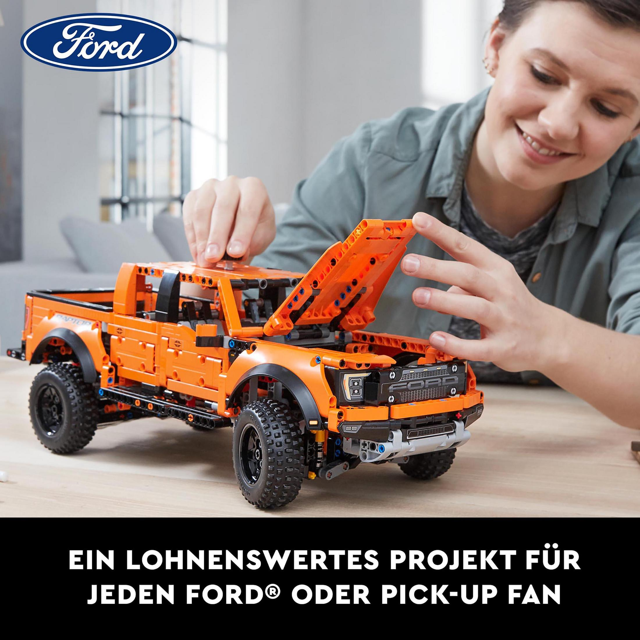 Frau baut Ford Pickup Truck Lego-Set zusammen. Oranger Lego-Truck auf Tisch.