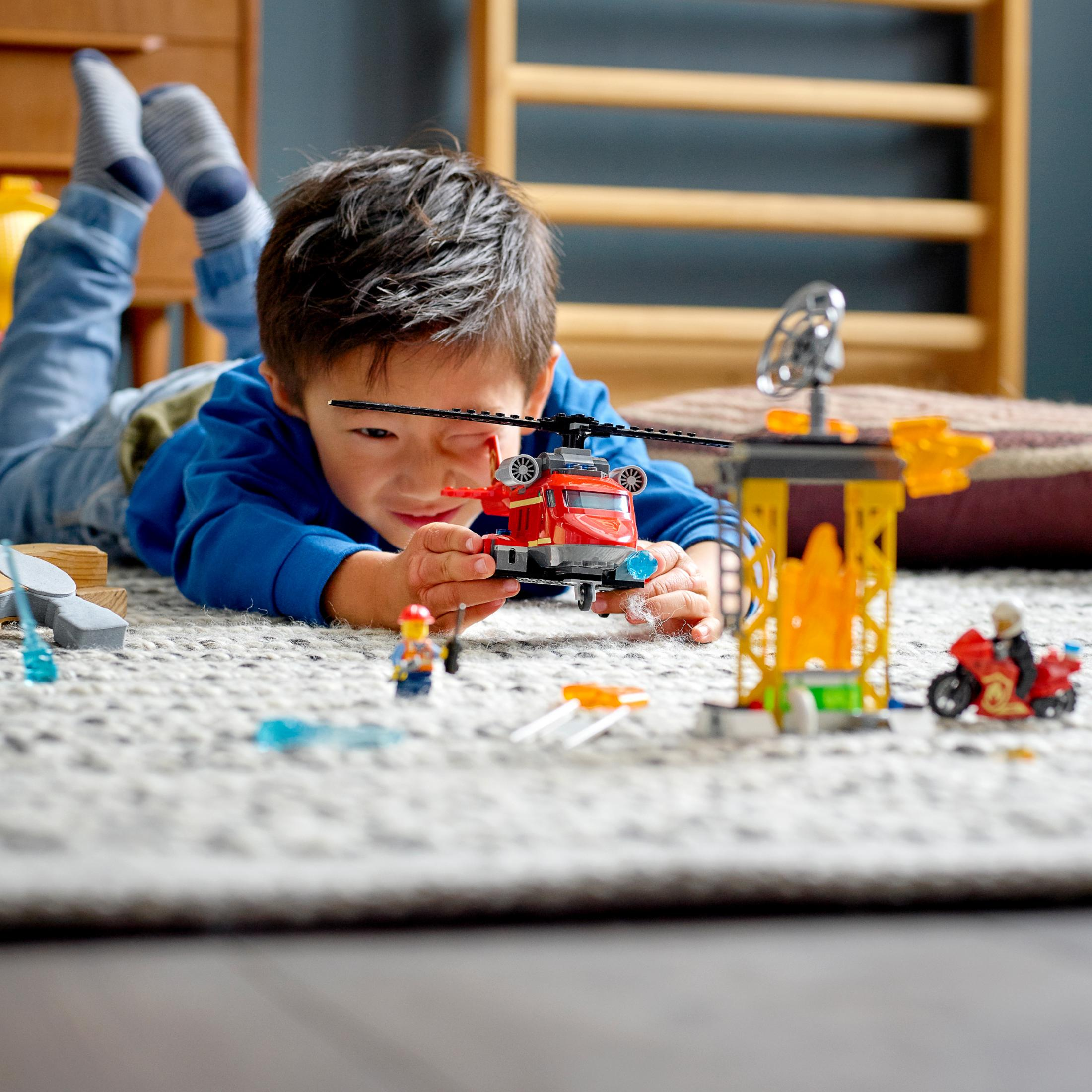 Junge spielt mit Lego-Hubschrauber und Figuren auf einem Teppich mit Holzregal im Hintergrund.