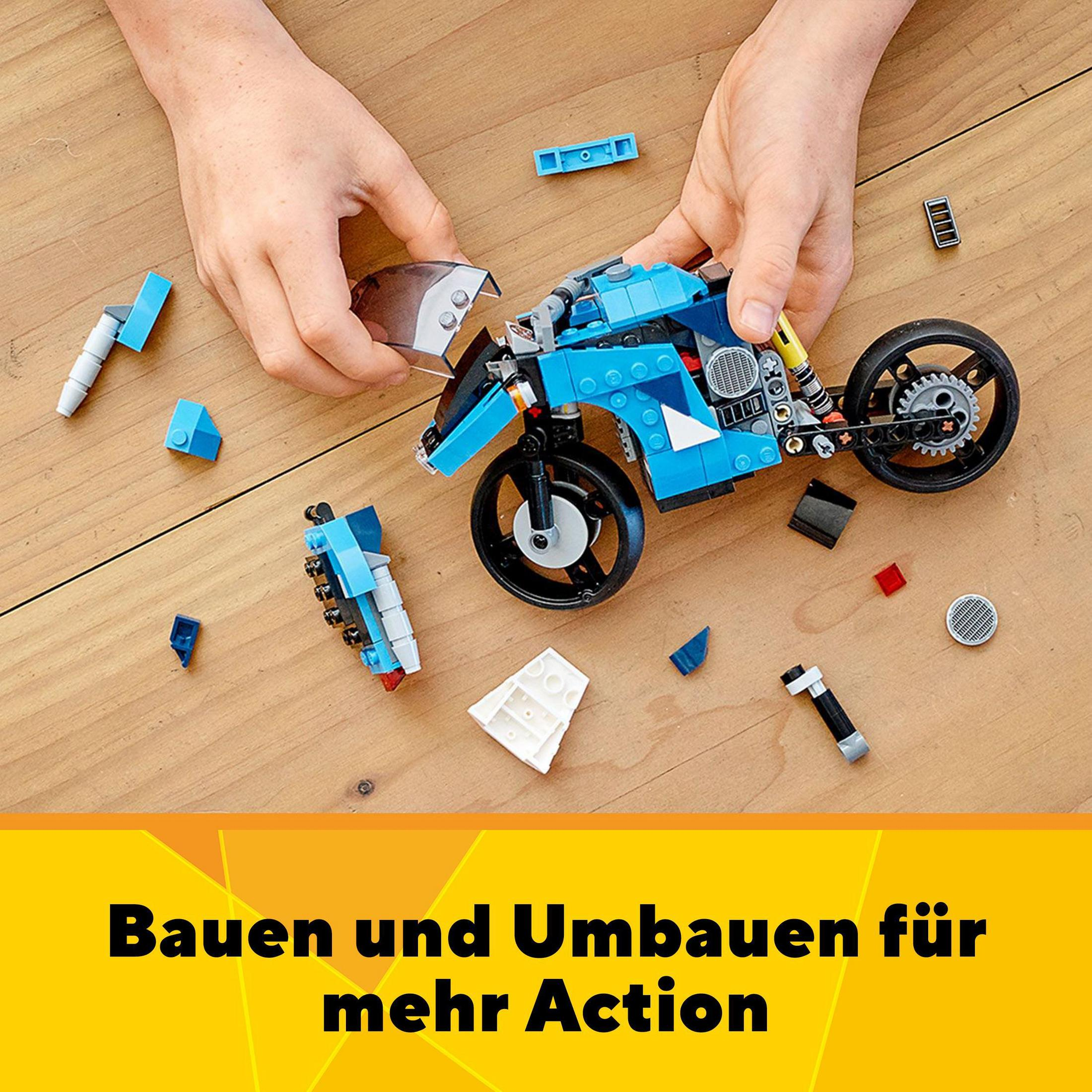 Hände bauen ein blau-weißes Lego-Motorrad auf Holzoberfläche. Andere Legoteile verstreut.