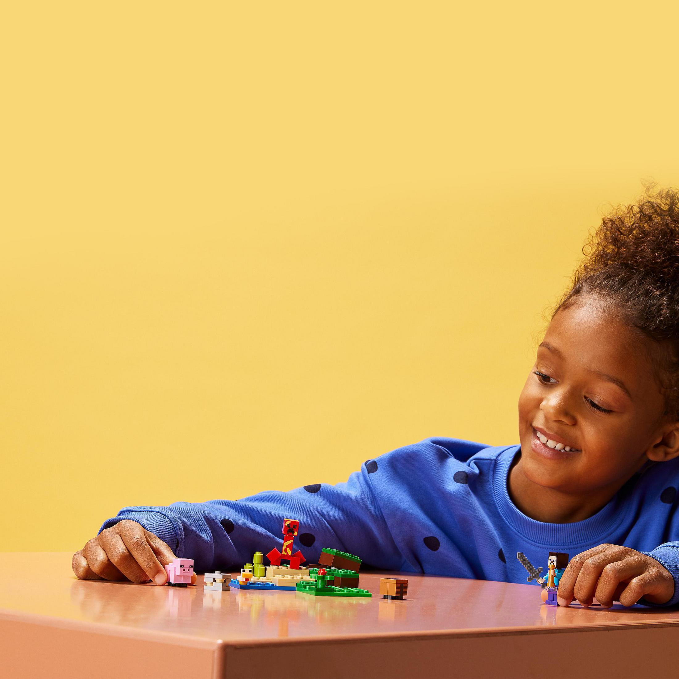 Bambino gioca con Lego, maiale rosa, blocchi e personaggi Lego sul tavolo.