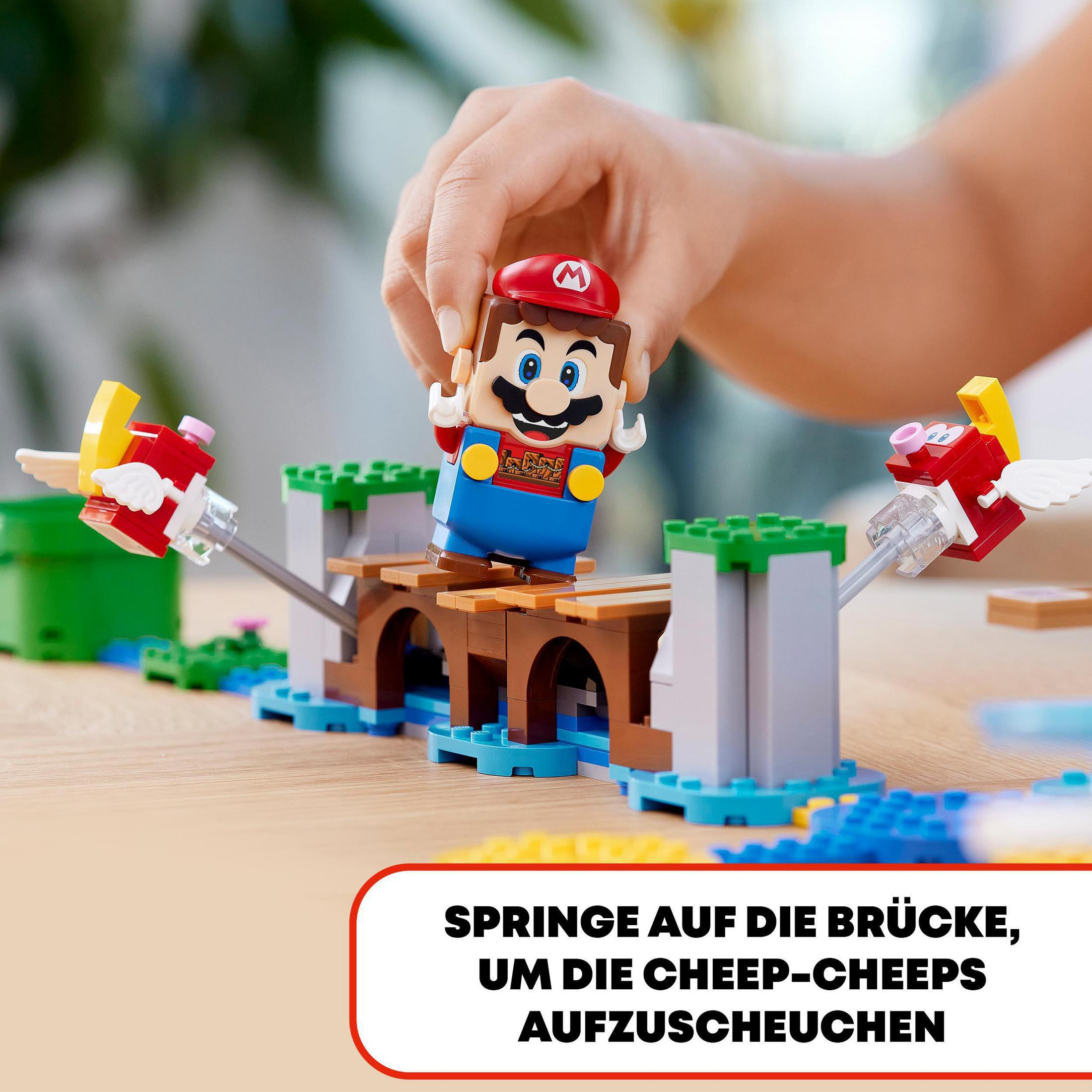 Eine Hand platziert eine Mario-Figur auf einer Lego-Brücke mit Cheep-Cheeps.