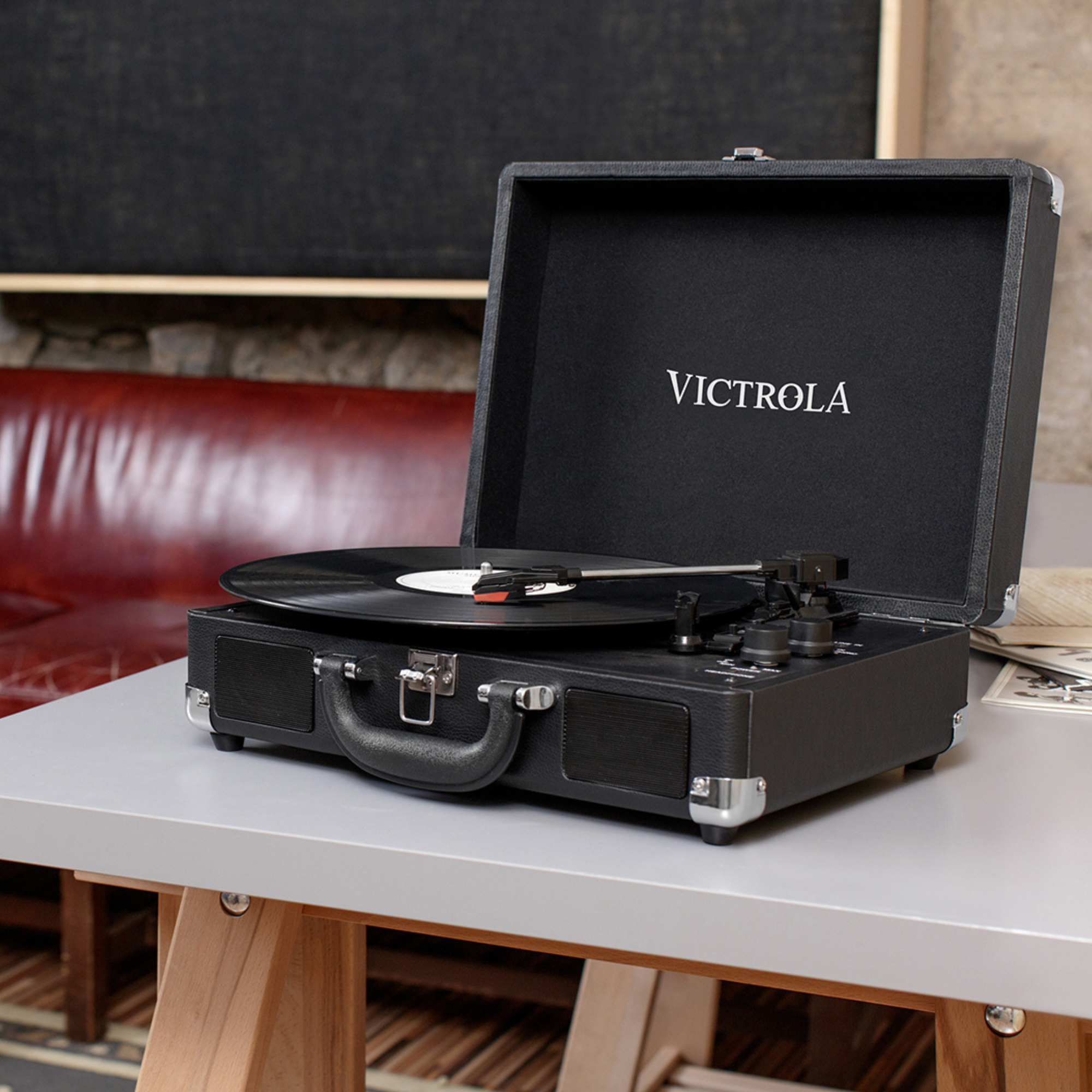 Un tocadiscos negro sobre una mesa gris. La tapa del tocadiscos está abierta, revelando un disco.