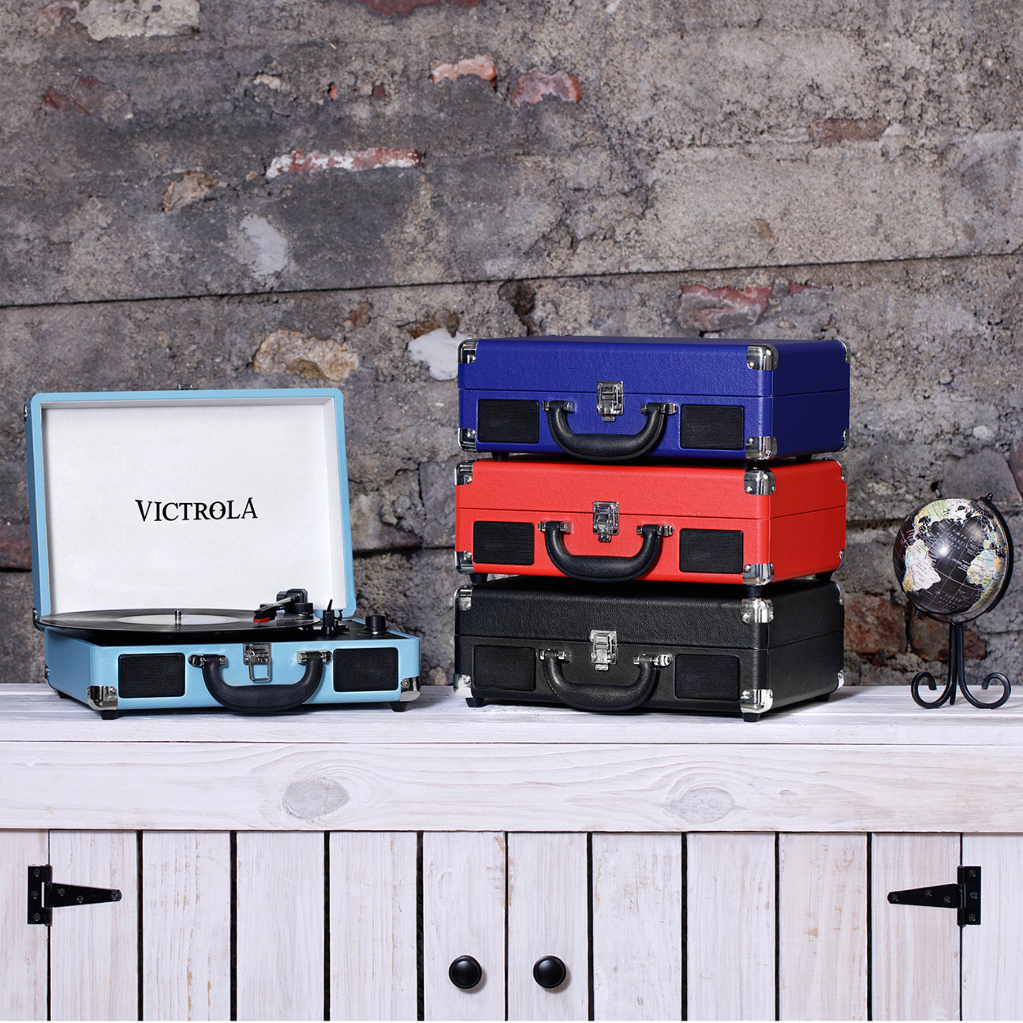 Tocadiscos y maletas apiladas sobre un mueble blanco con un globo terráqueo.