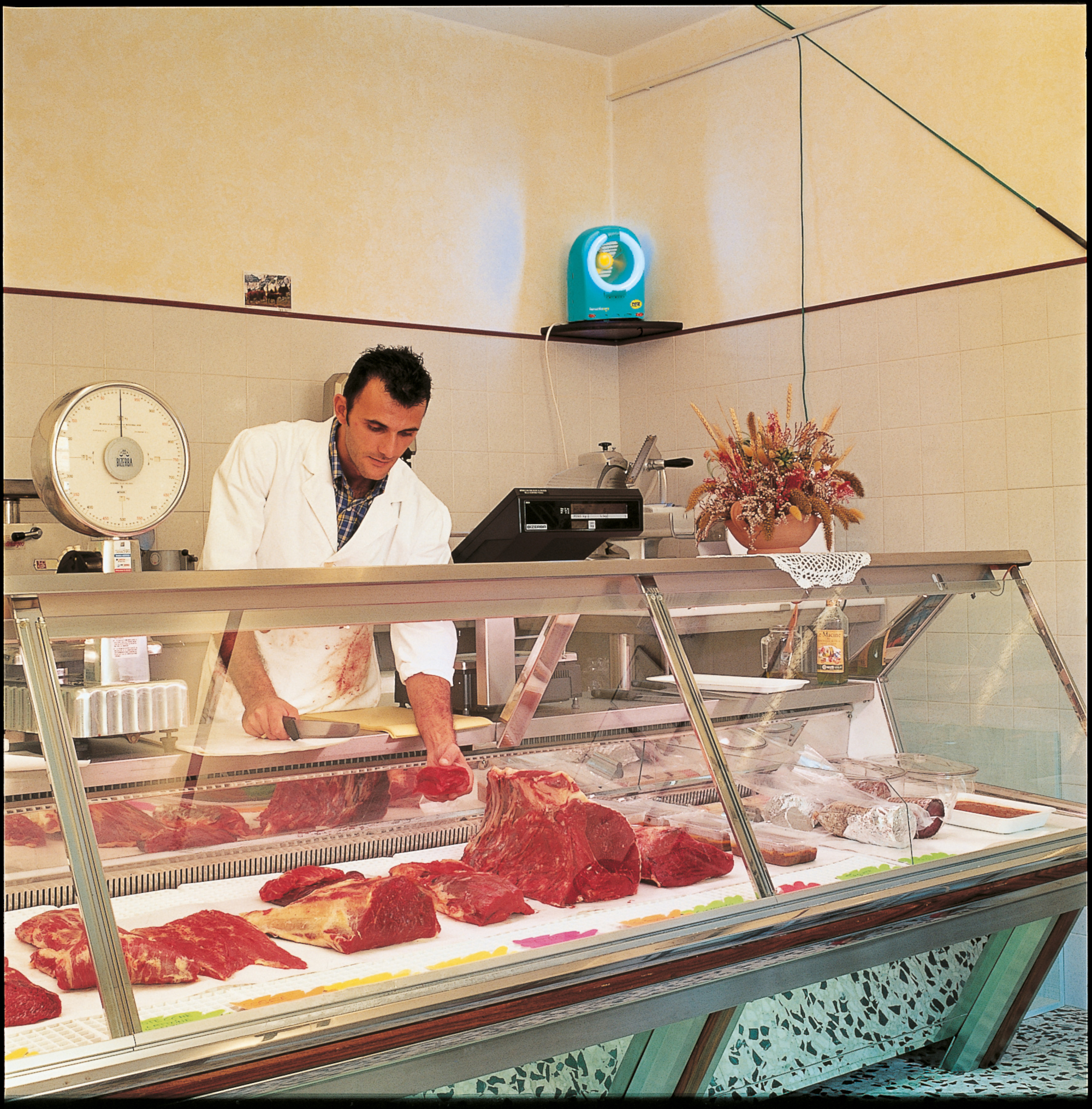Eine Metzgerei mit einem Metzger, der Fleisch hinter einer Glasvitrine schneidet. Verschiedene Fleischsorten werden ausgestellt.