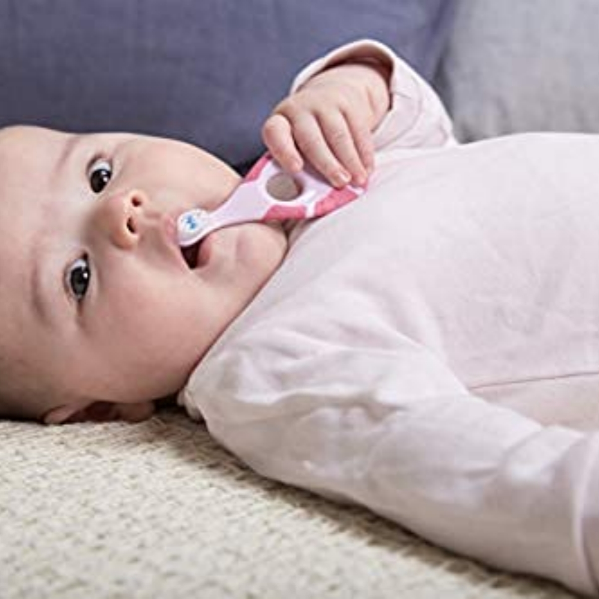 Baby liegt auf einer Decke, hält einen rosa Beißring im Mund und schaut mit großen Augen nach oben.