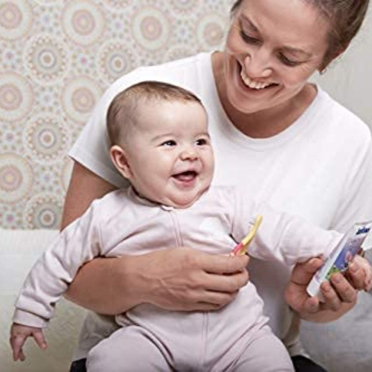 Eine Mutter hält ein Baby. Beide lächeln, während das Baby eine Zahnbürste hält.