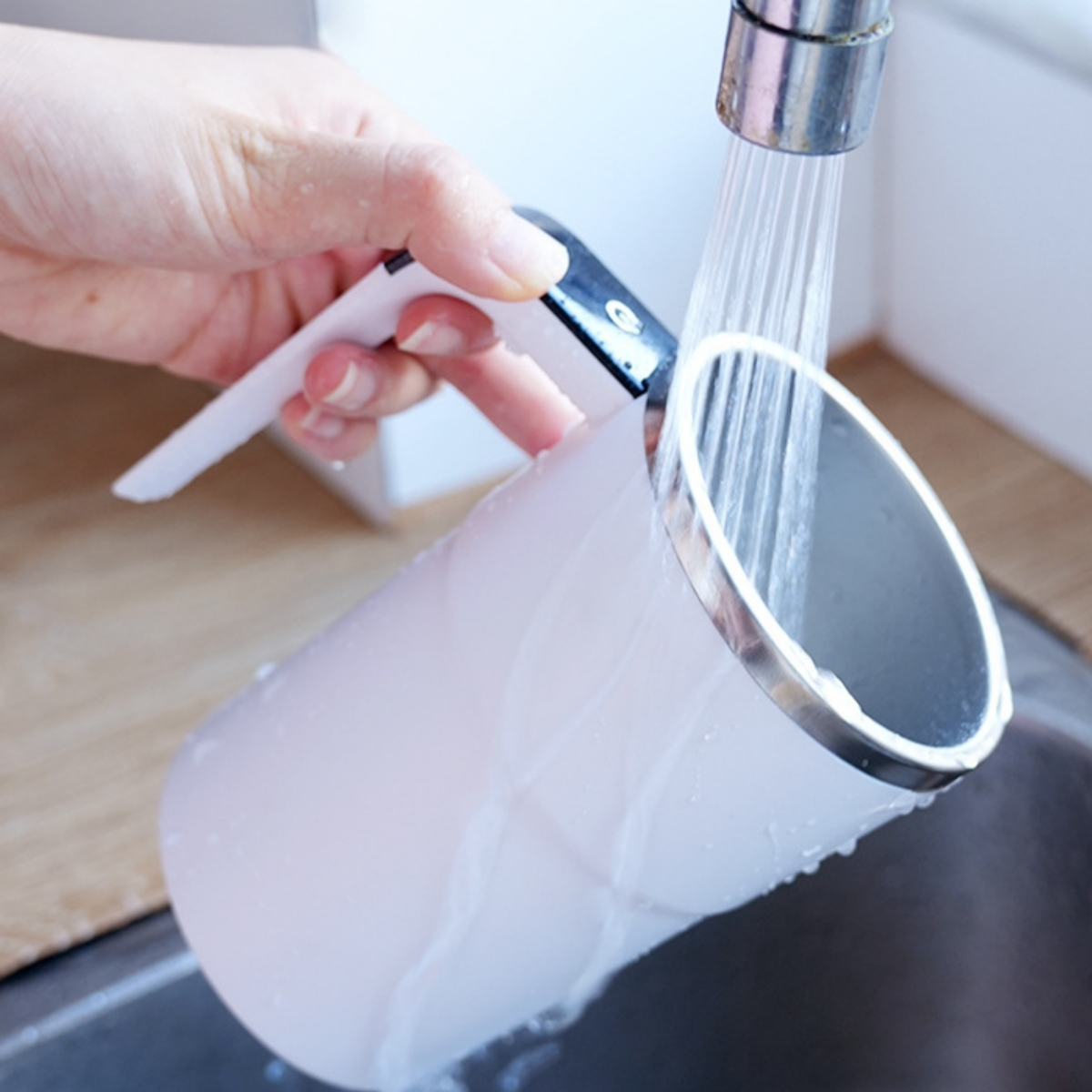 Weiße Tasse wird unter fließendem Wasser gespült. Silberner Rand, dunkler Innenraum.
