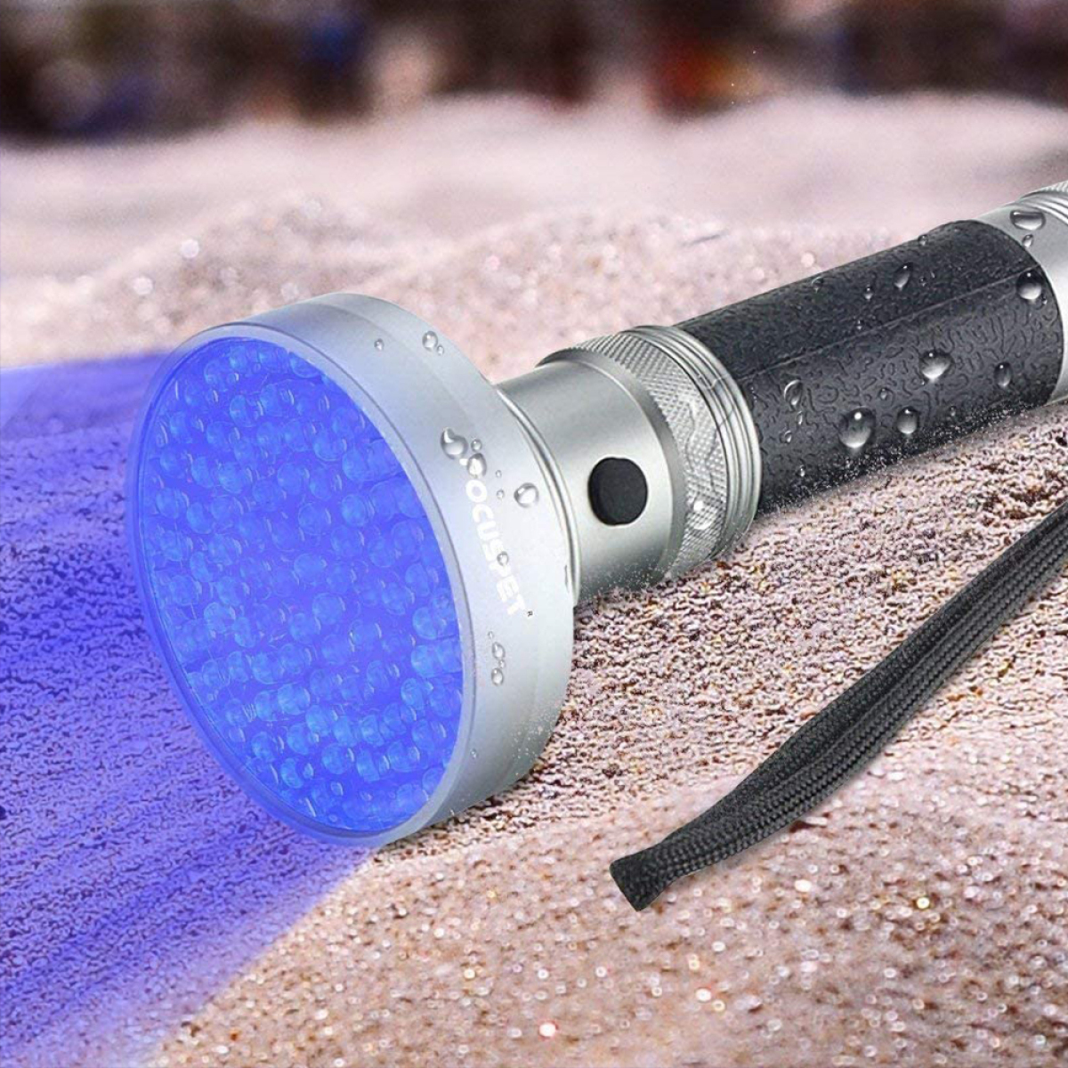 Eine schwarze UV-Taschenlampe, die blaues Licht auf einer sandigen Oberfläche aussendet.