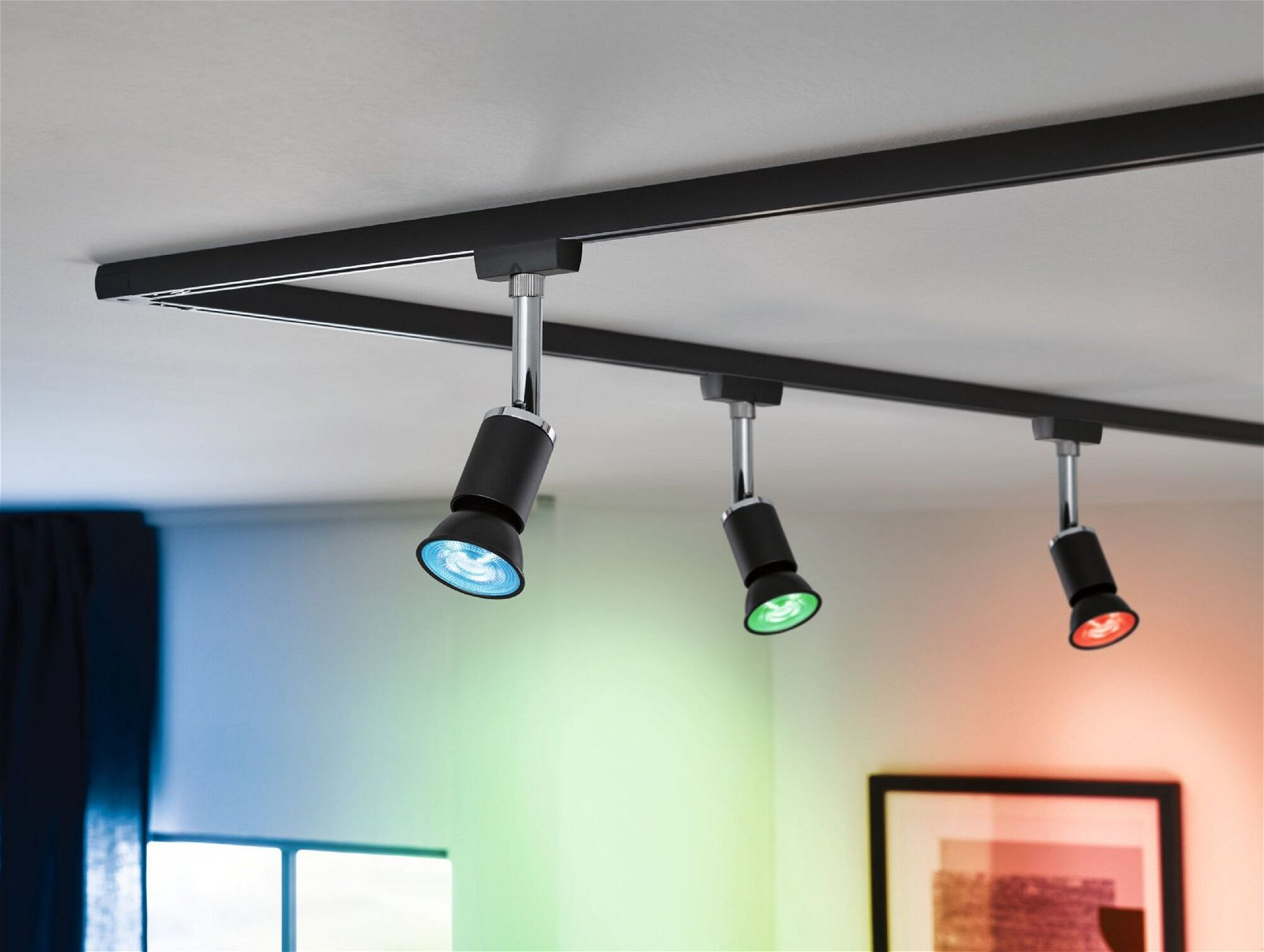 Deckenstrahler. Drei schwarze Strahler mit farbigem Licht an einer schwarzen Schiene.