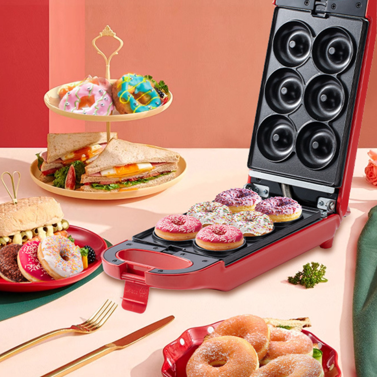 Ein roter Donut-Maker mit einer Schale mit gebackenen Donuts. Donuts werden auf Tellern zusammen mit Sandwiches präsentiert.