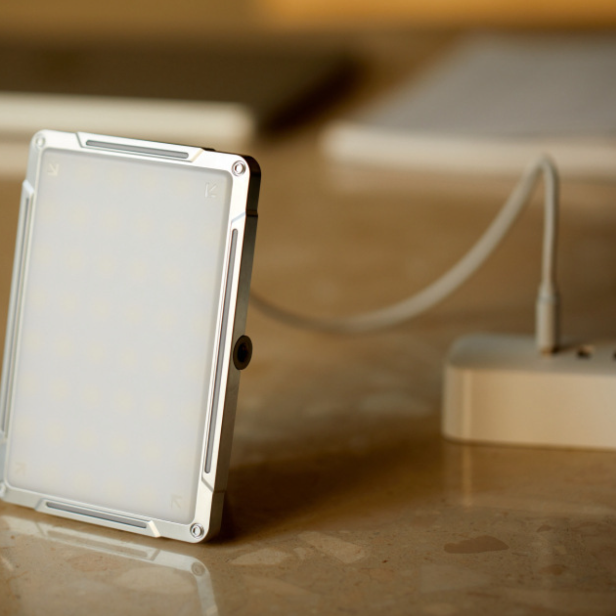 Silbernes LED-Lichtpanel, über ein weißes Kabel mit einem weißen Netzteil verbunden, auf Holzoberfläche.