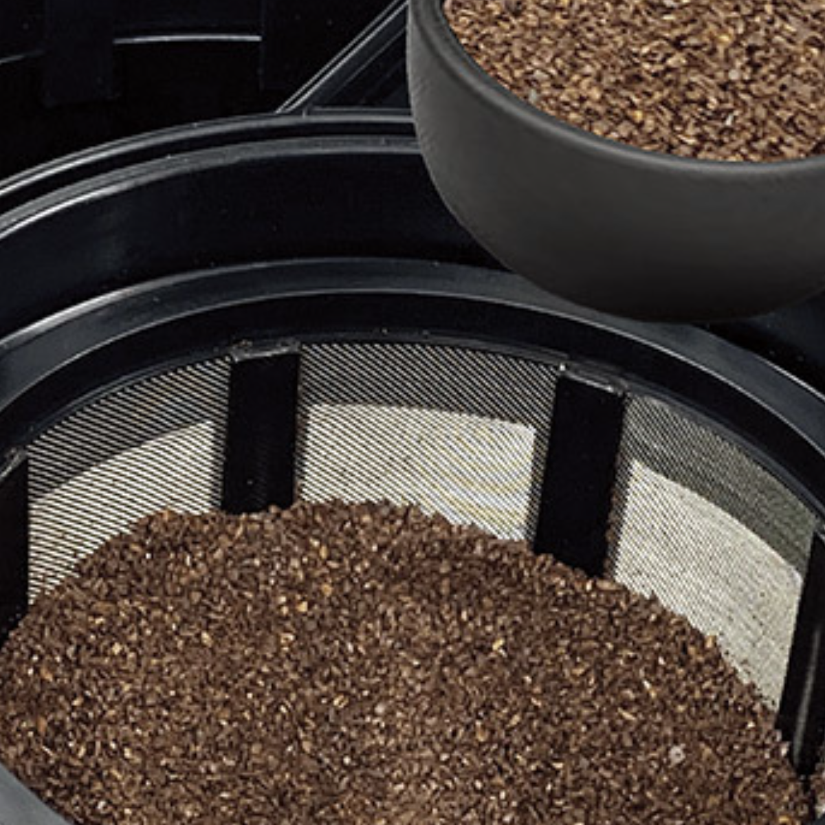 Nahaufnahme von Kaffeepulver in einem Filter, mit einer schwarzen Schüssel obenauf.