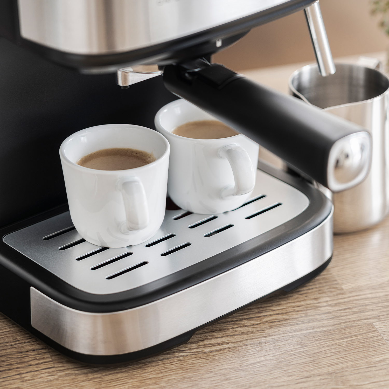 Espressomaschine mit zwei weißen Tassen Kaffee und einem Milchkännchen.