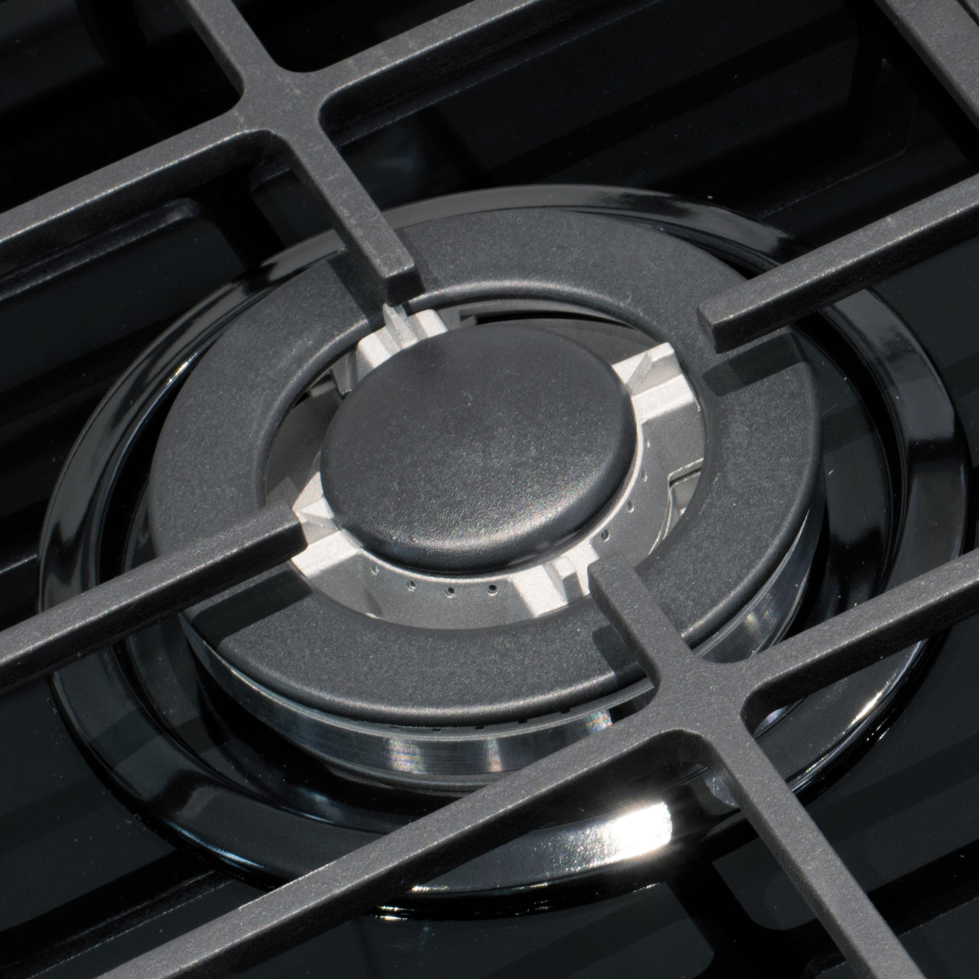 Zbliżenie palnika kuchenki gazowej z czarną kratką. Palnik jest srebrny, z czarnym pierścieniem wokół niego.